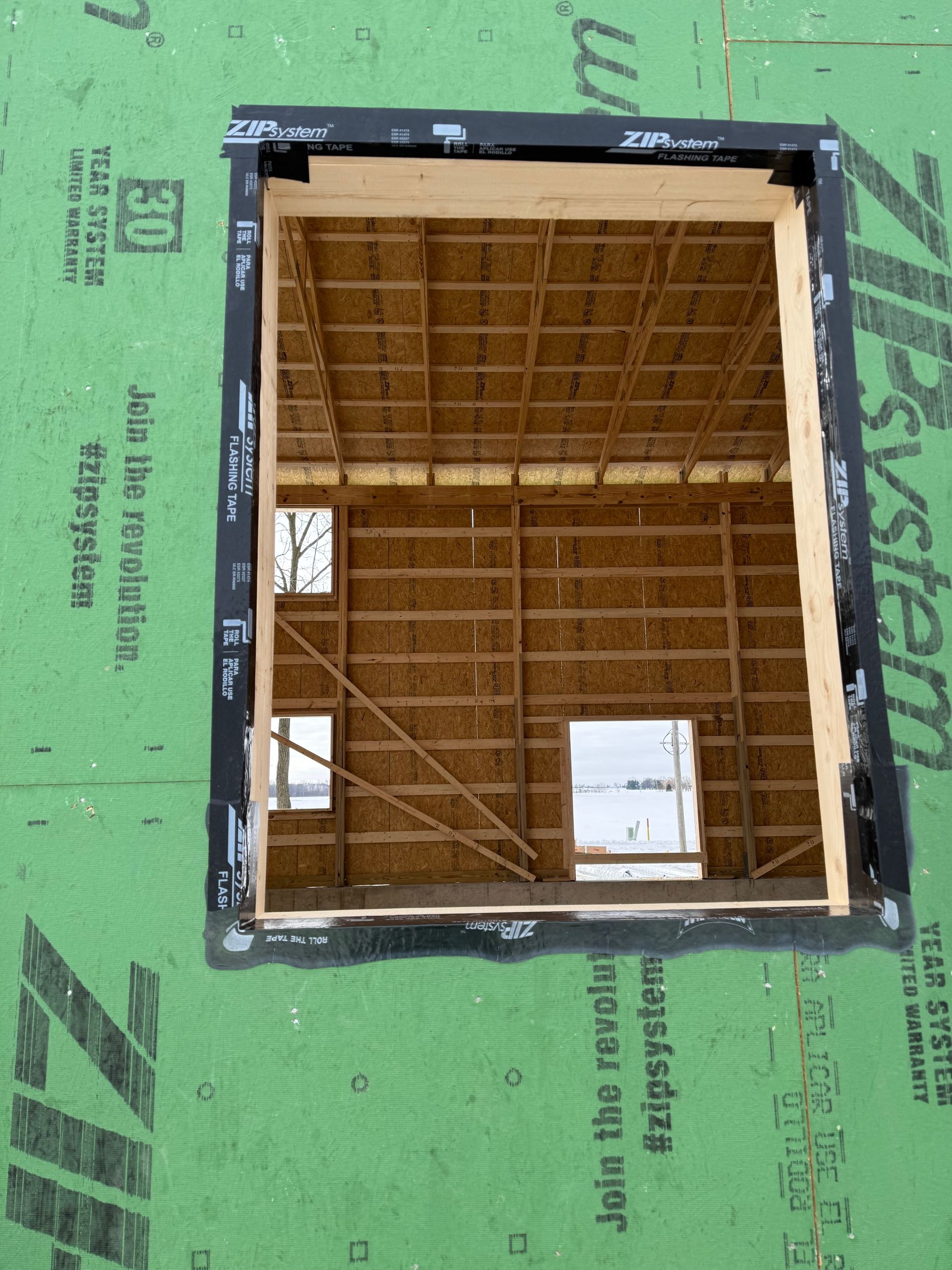 Open wall framing with plywood roof and black window flashing on green house wrap