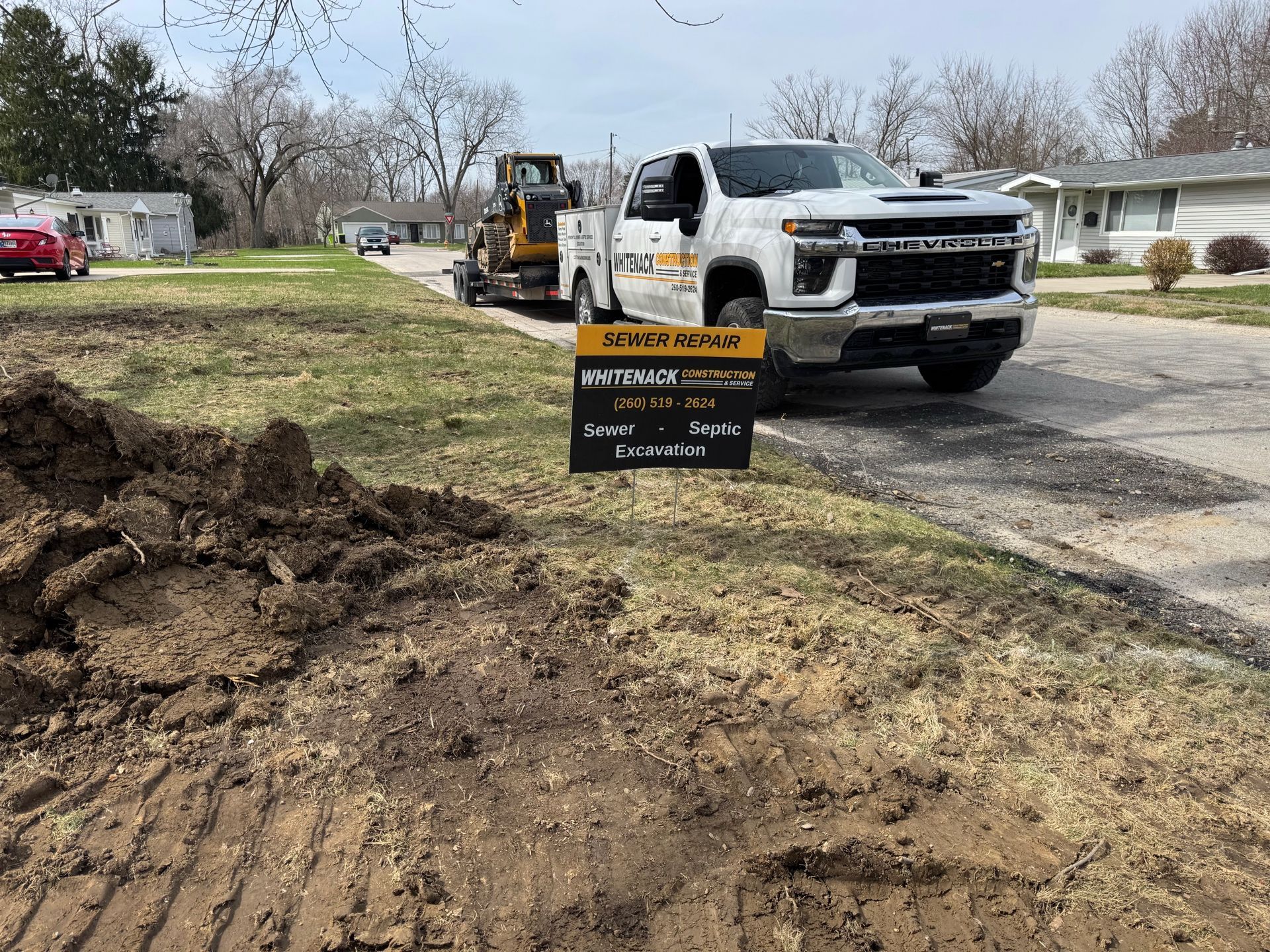 Construction vehicles working beside a muddy road, with a no-trespassing sign in the foreground.