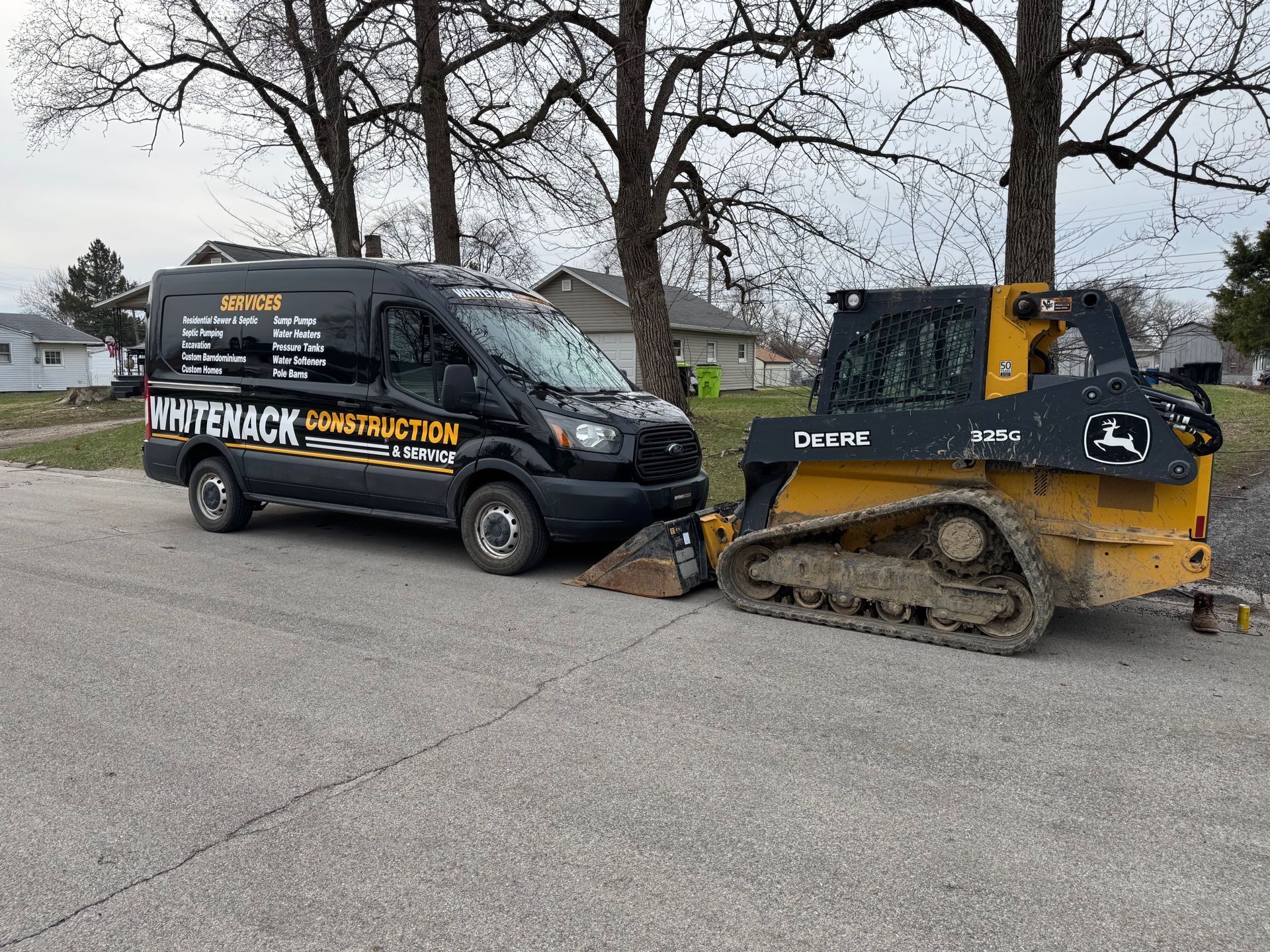Black HAVENKAK truck and yellow skid steer push together on a suburban street.