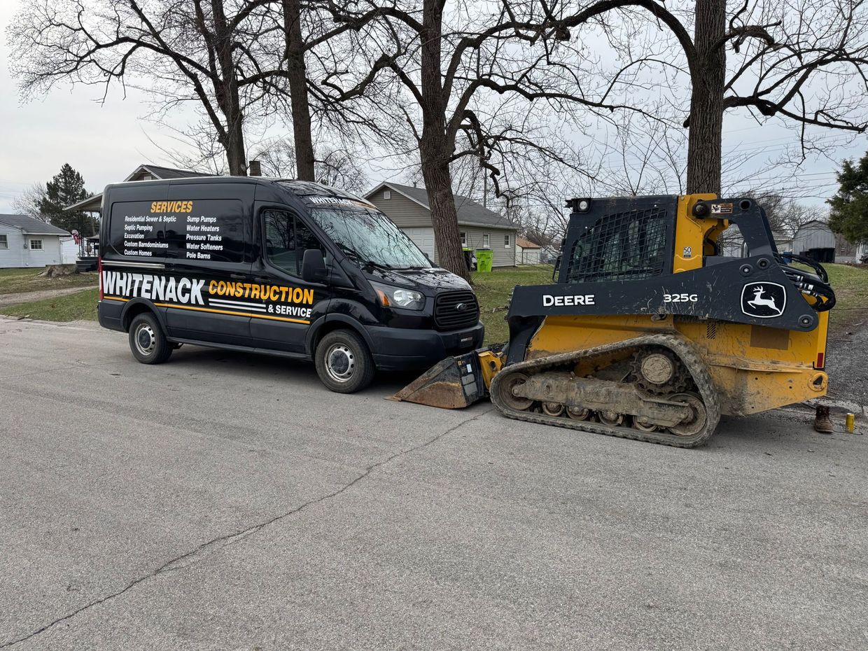 Black van and yellow skid steer in a residential street blocking a damaged driveway.