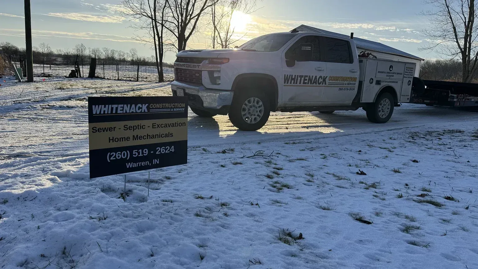 Pickup truck parked in snowy field beside a white sign at sunset