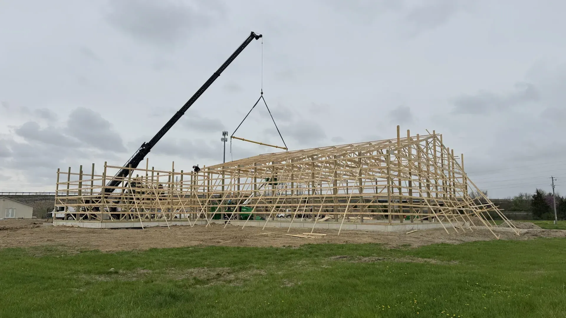 Crane lifting wooden roof trusses at a house under construction on a cloudy day
