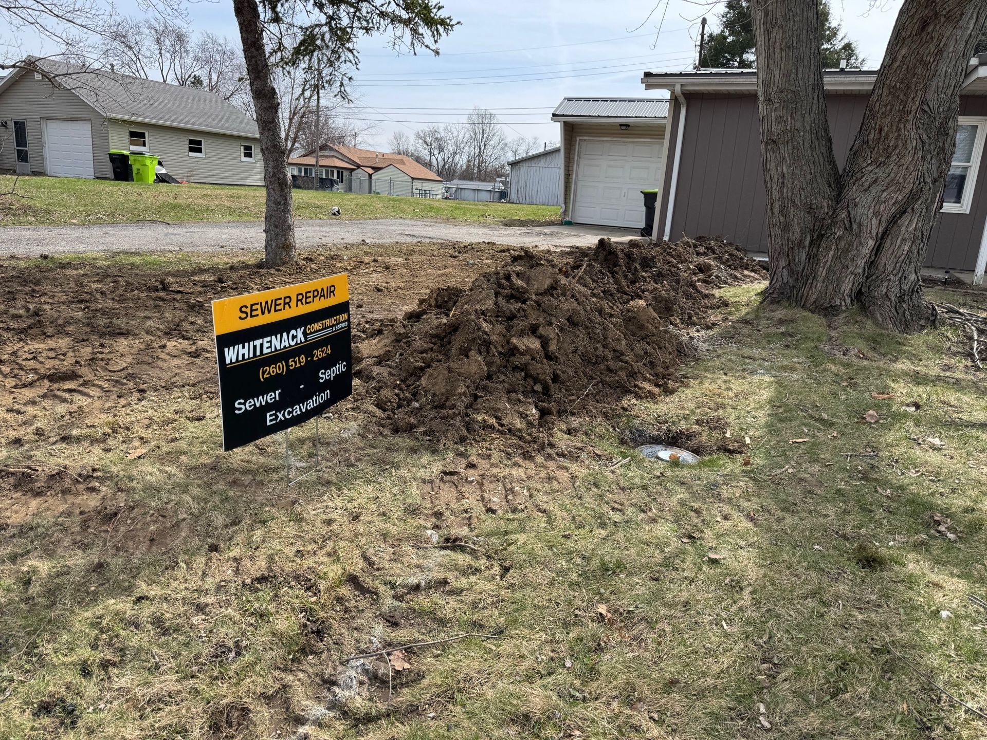 Yard sign beside a muddy excavation trench next to a house and tree in a suburban yard