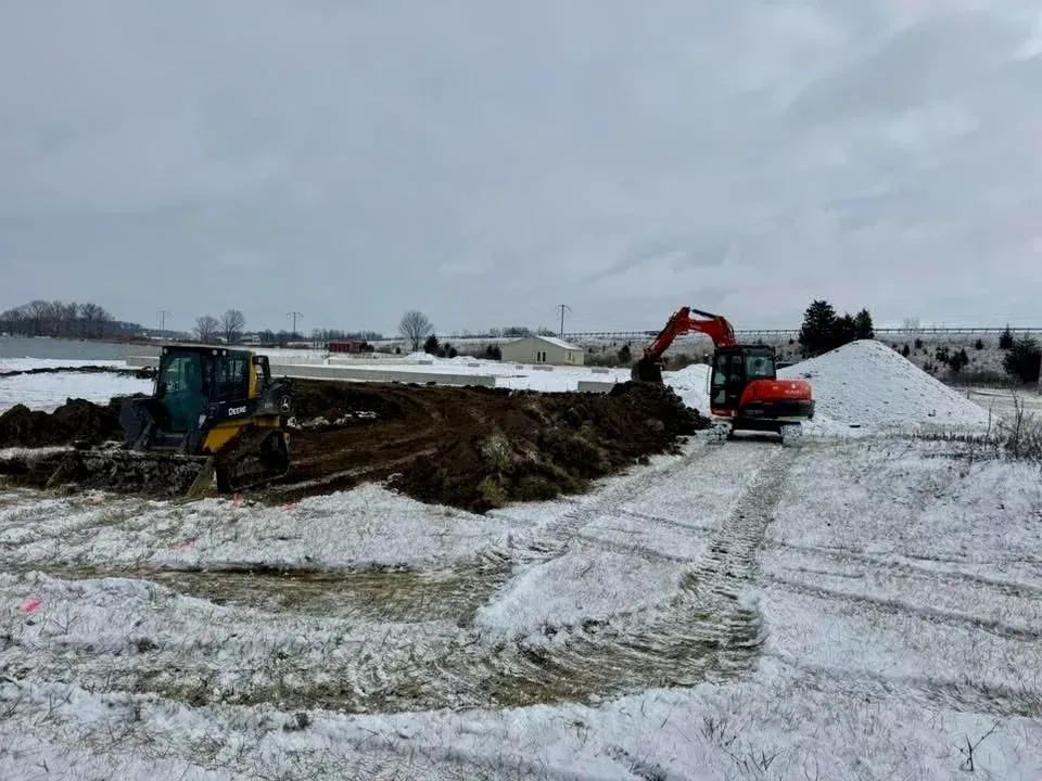 Construction machinery working in a snowy excavation site under an overcast sky