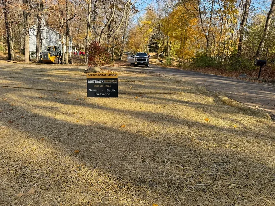 Gravel campground with a sign in front of a parked SUV and autumn trees