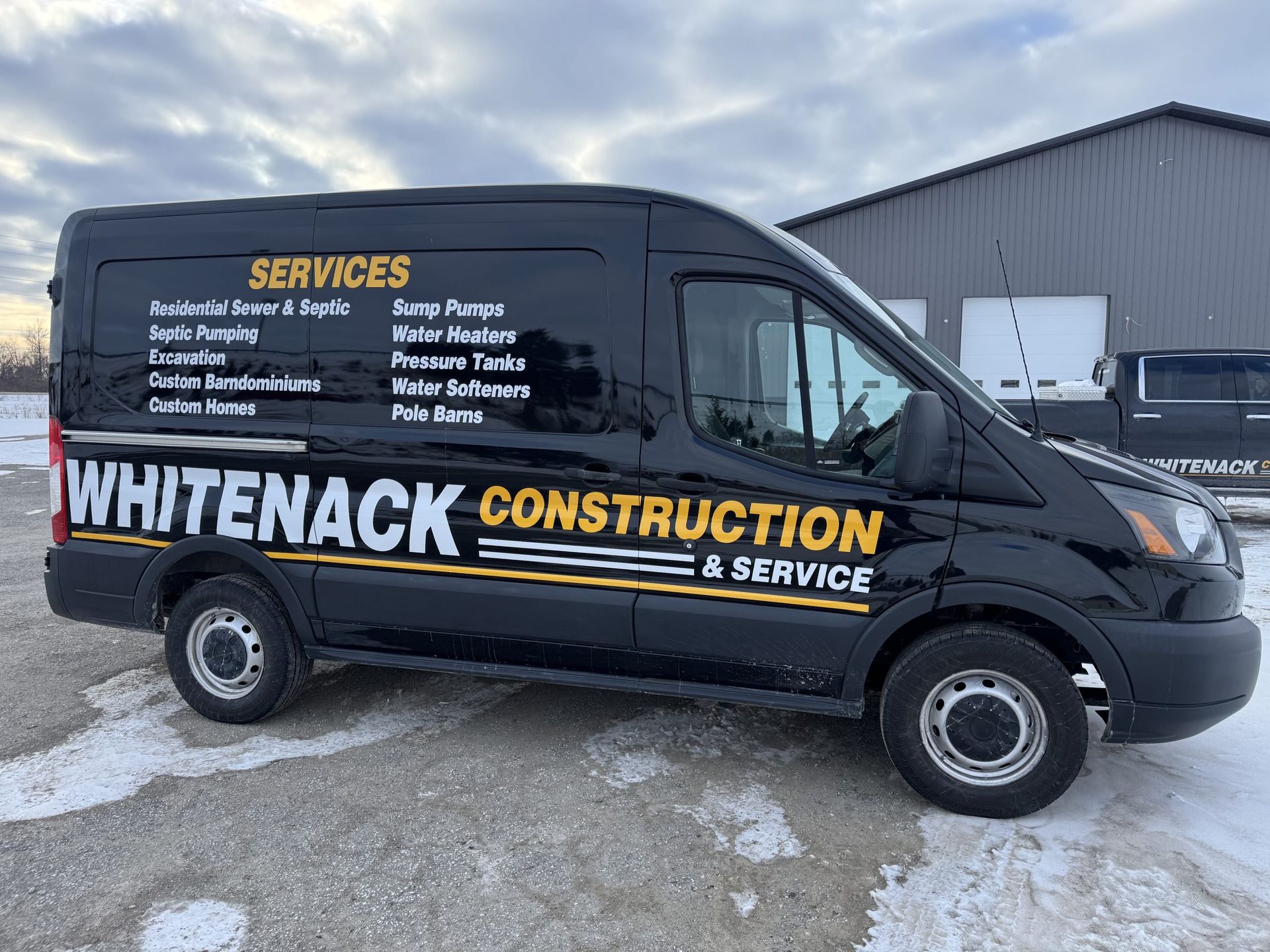 Black Whitenack Construction service van parked on snowy pavement beside a gray building