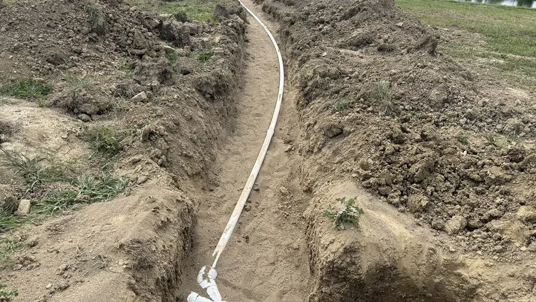 White pipe runs through a dry, rocky dirt trench on a hillside.