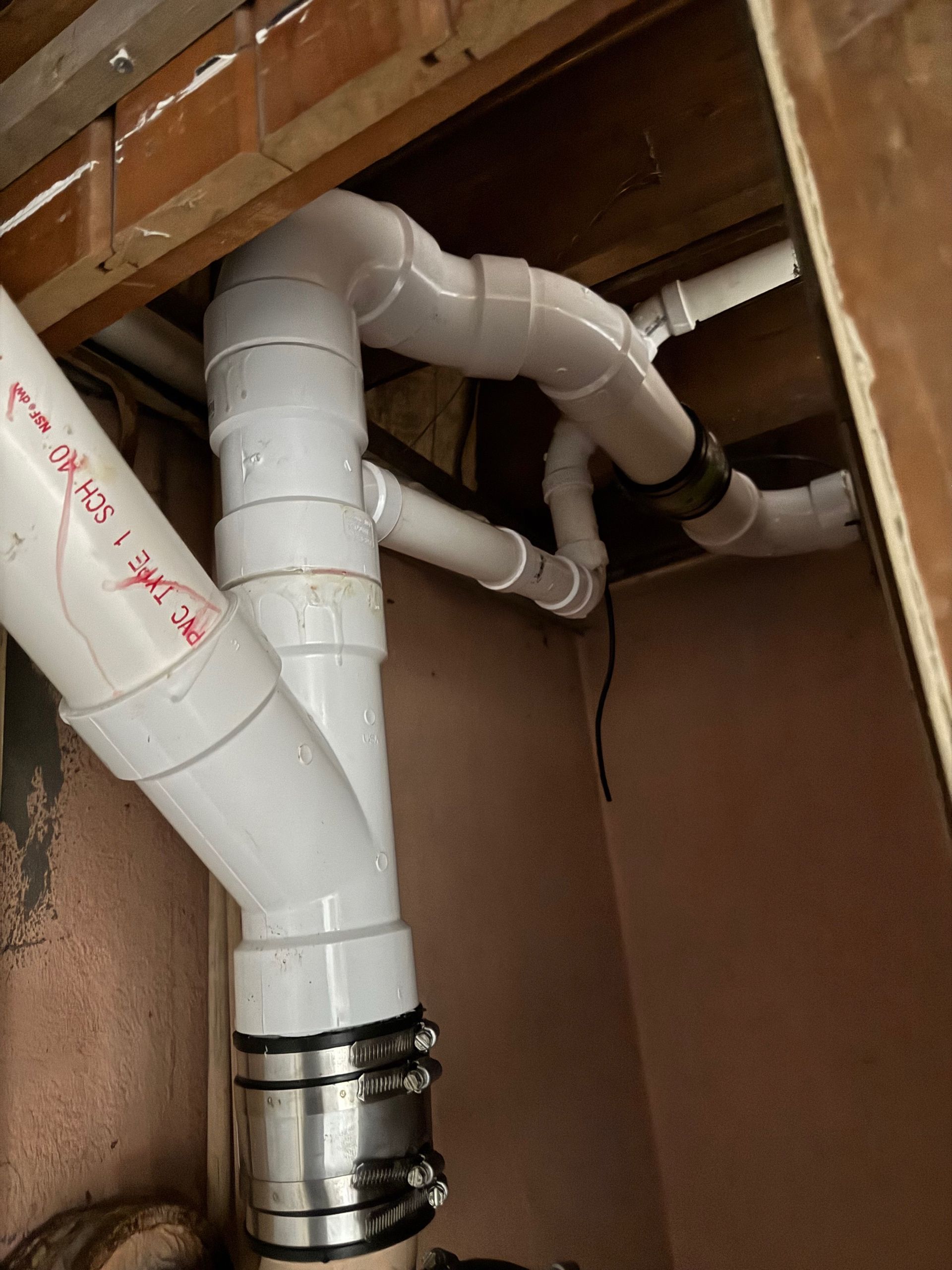 White PVC plumbing pipes installed under a sink or in a cabinet, with metal clamps and exposed framing