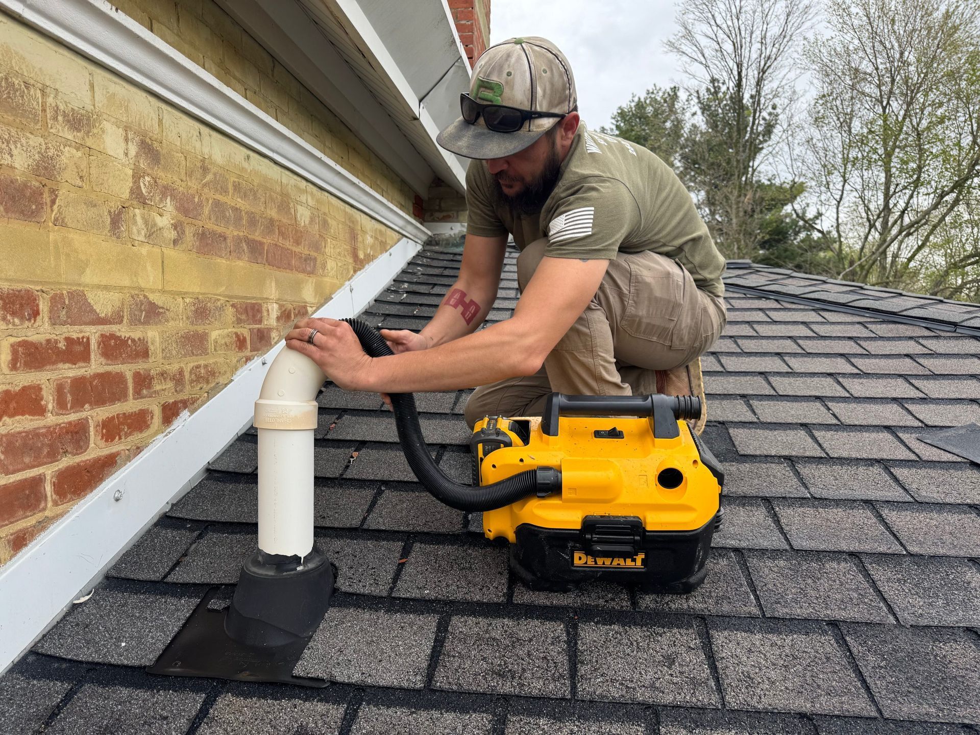 Worker installing roof shingles near white vent pipe on a house roof