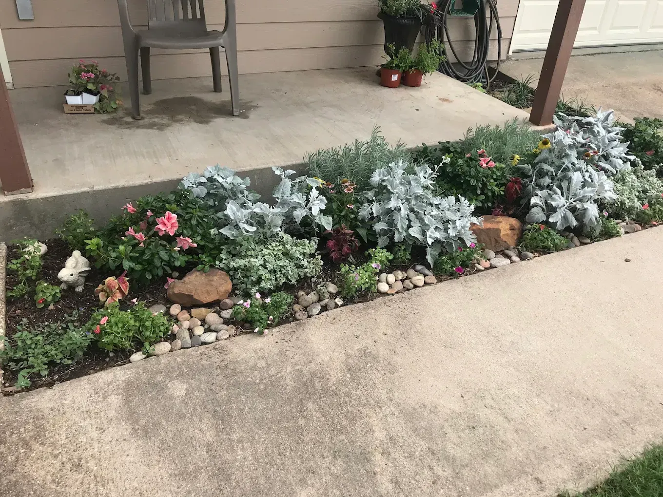 Small front porch garden bed with white, pink, and red flowers along a concrete walkway