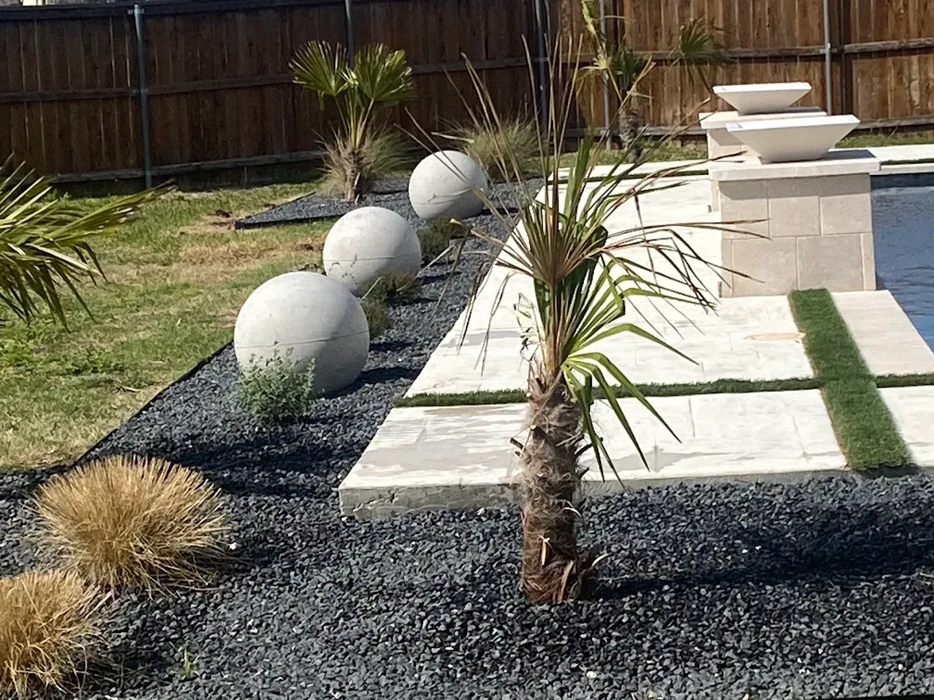 Modern backyard with white stone pavers, black gravel, and decorative white spheres along a fence