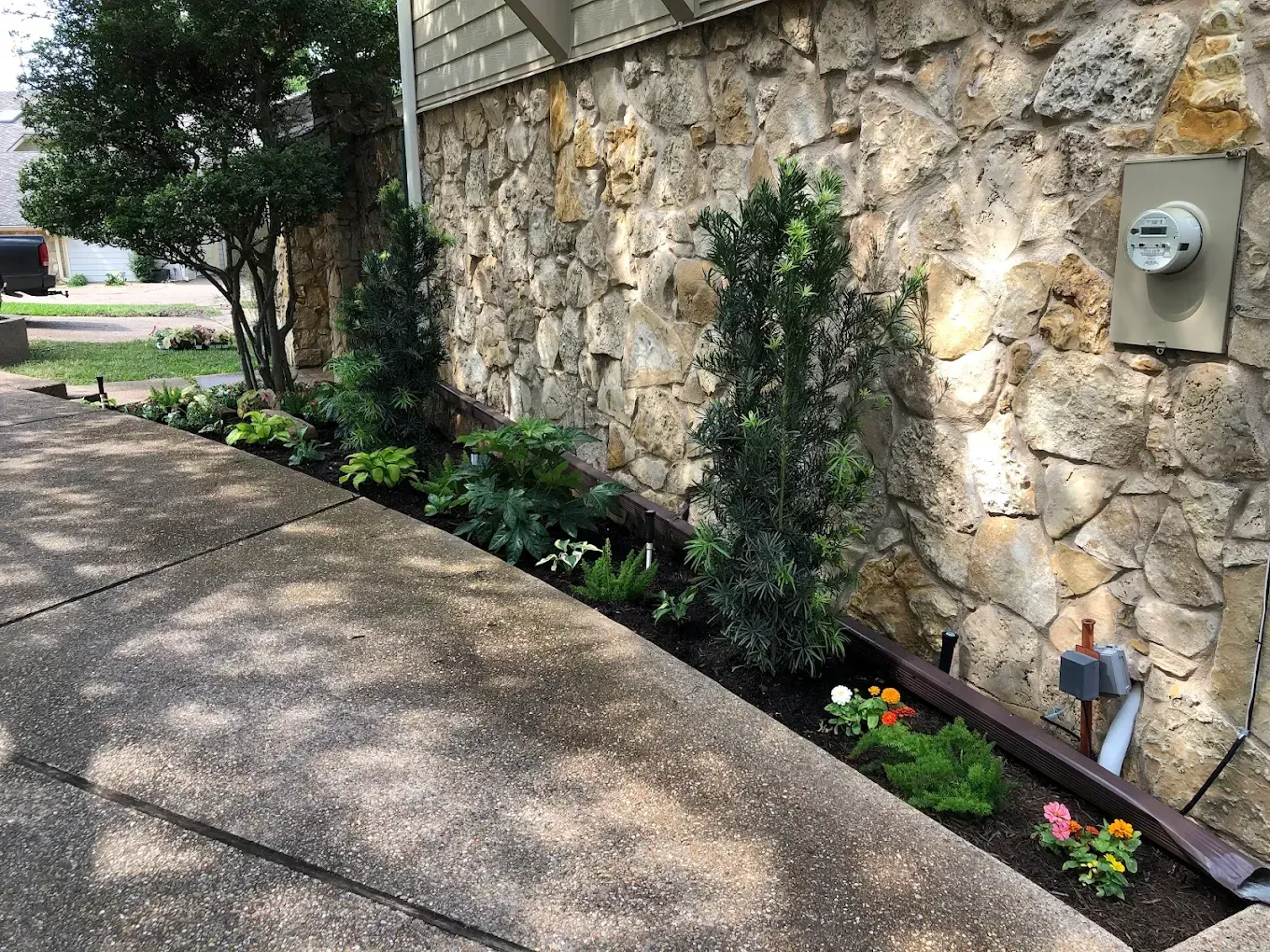 Curved sidewalk beside a stone wall with a flower bed of pink, yellow, and white blooms