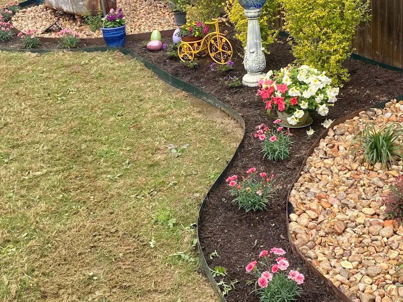 Curved garden border with flowers, rocks, and decorative wheelbarrow beside a lawn