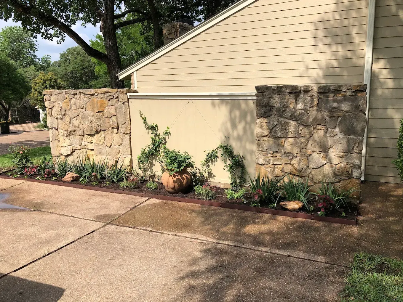 Stone and stucco house exterior with landscaped flower bed beside a driveway