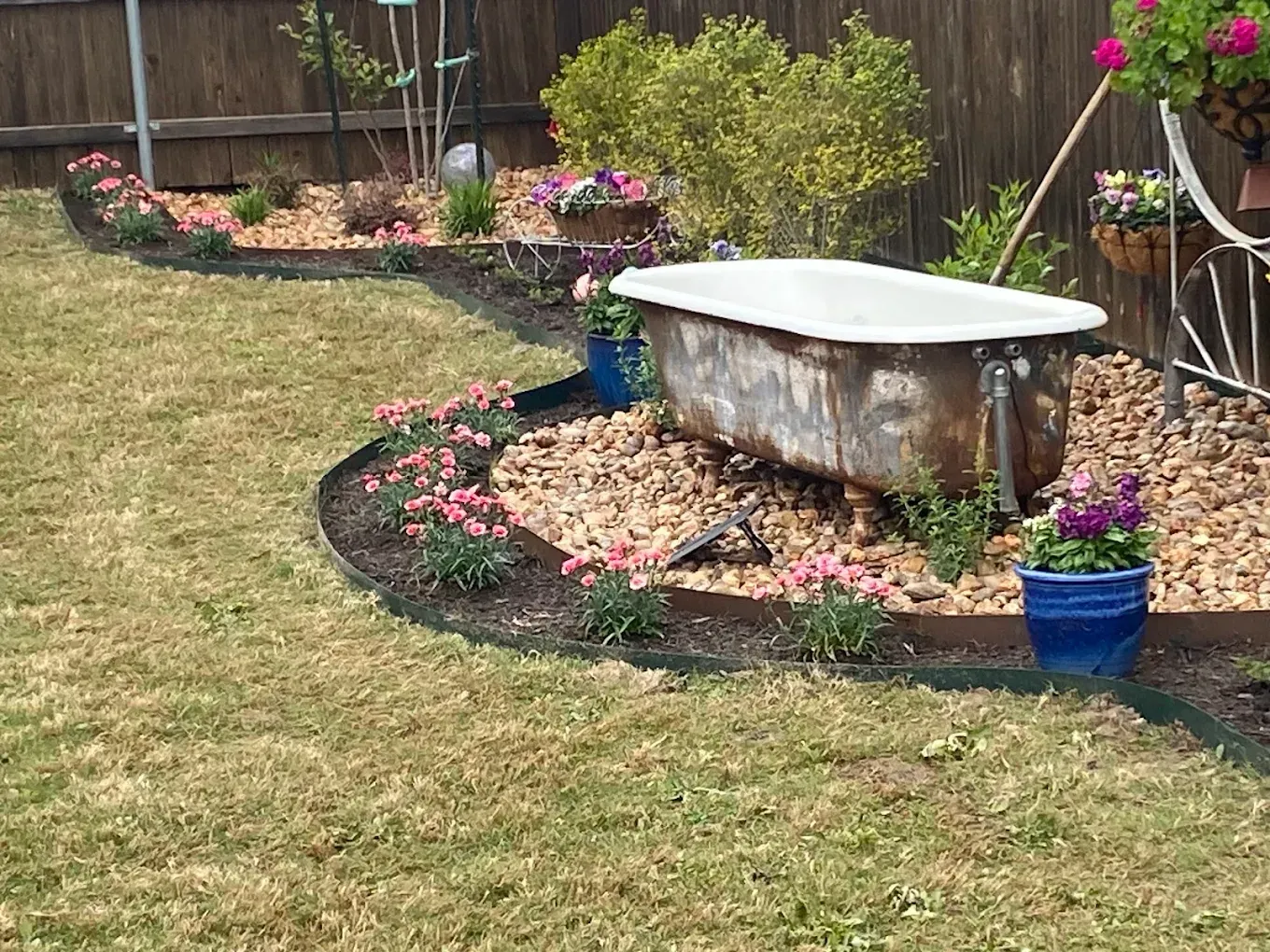 Backyard garden with a white bench, pink flowers, blue planters, and a curved stone bed
