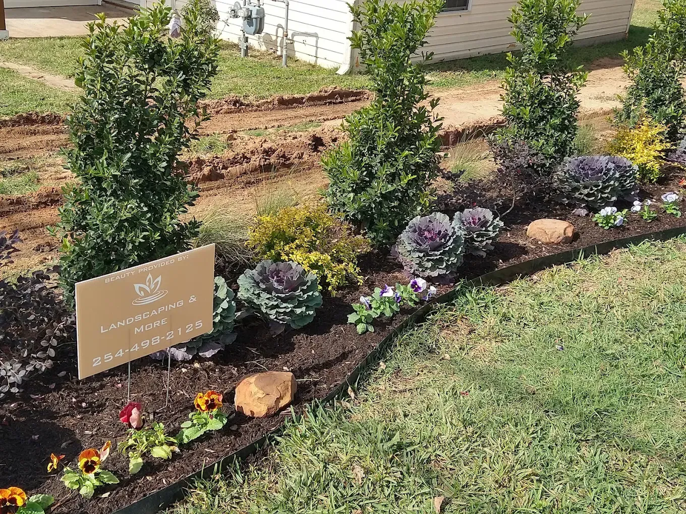 Landscaped memorial garden with flowers, shrubs, mulch, and a commemorative plaque sign