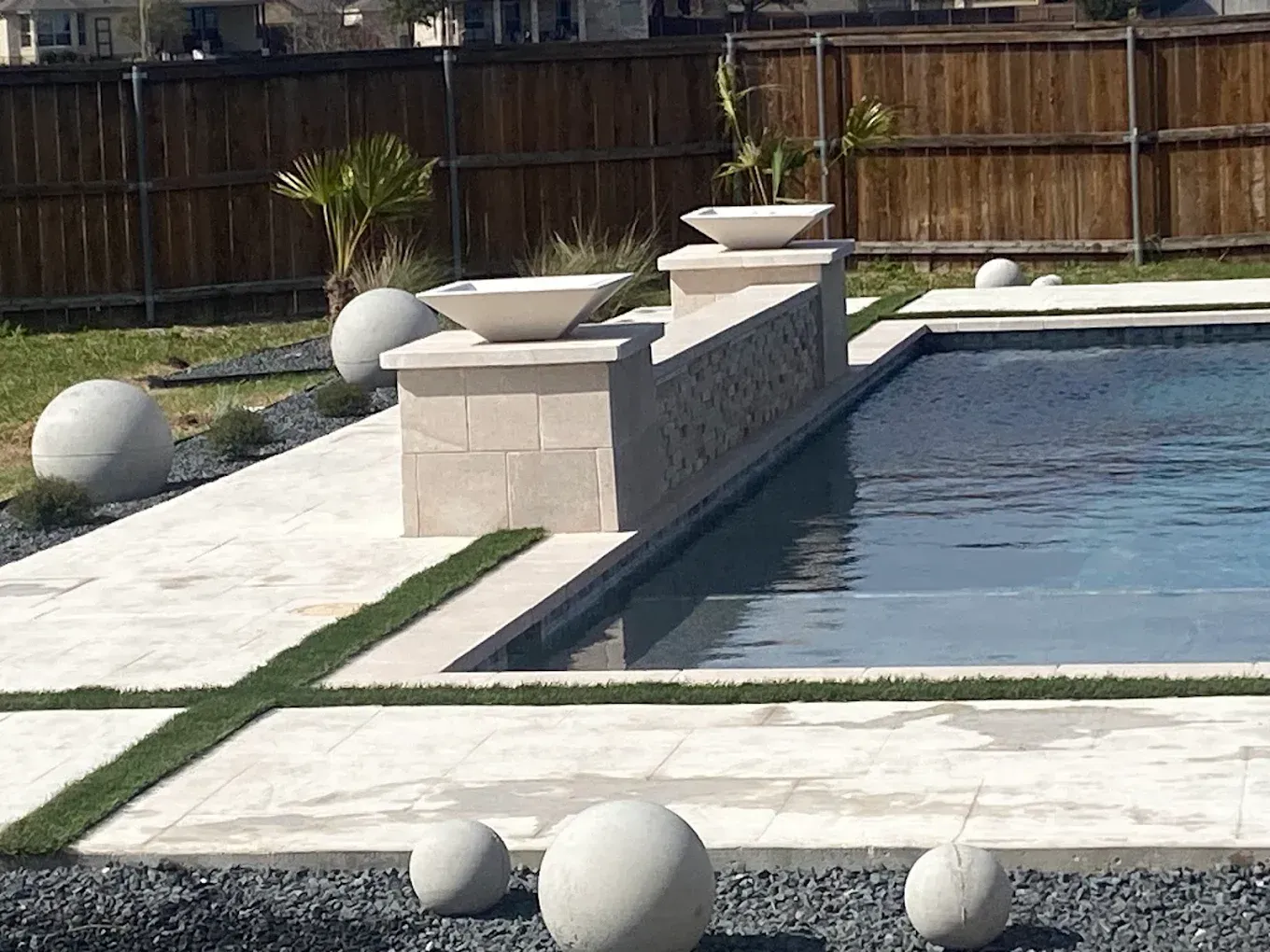 Backyard swimming pool with a stone water feature and white decorative spheres on the patio