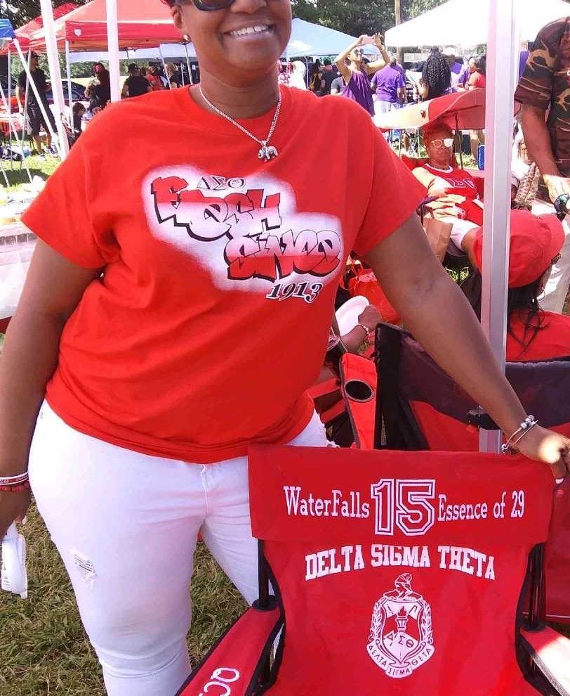 A woman wearing a delta sigma theta shirt stands next to a red chair
