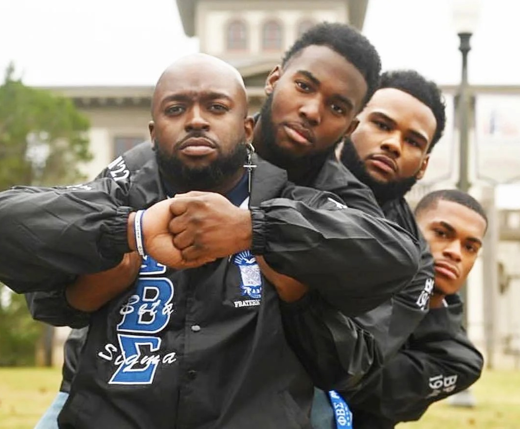 A group of men are posing for a picture and one of them is wearing a jacket that says nba