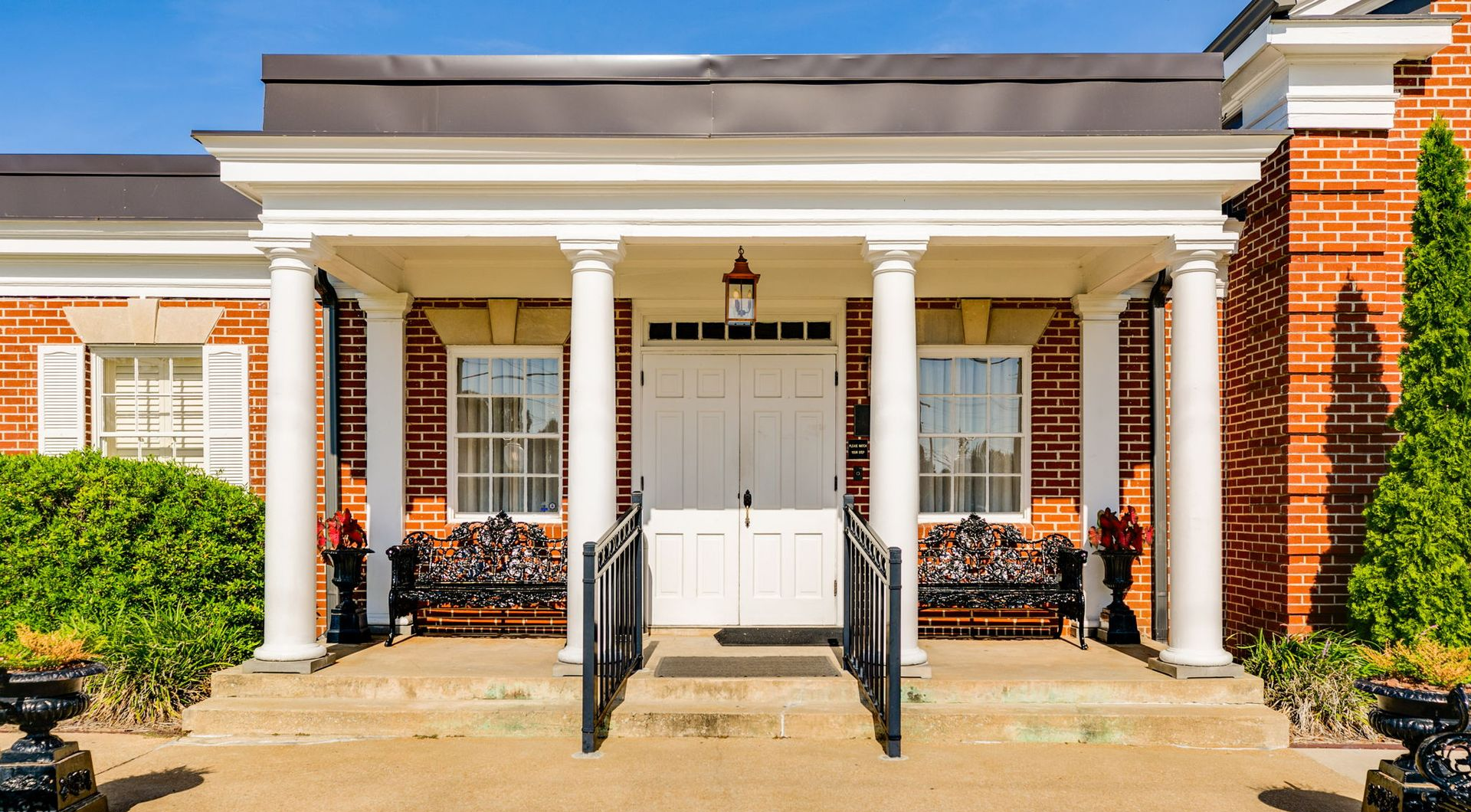 White-columned brick house entrance with front porch, black railings, and double doors