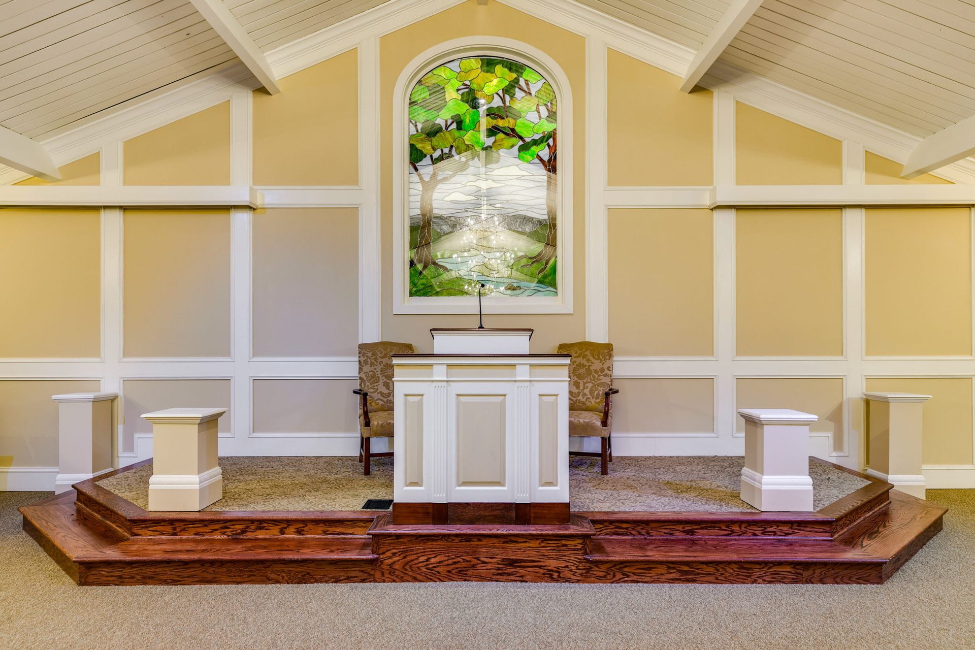 Small church altar with white podium, red carpet, and stained-glass window