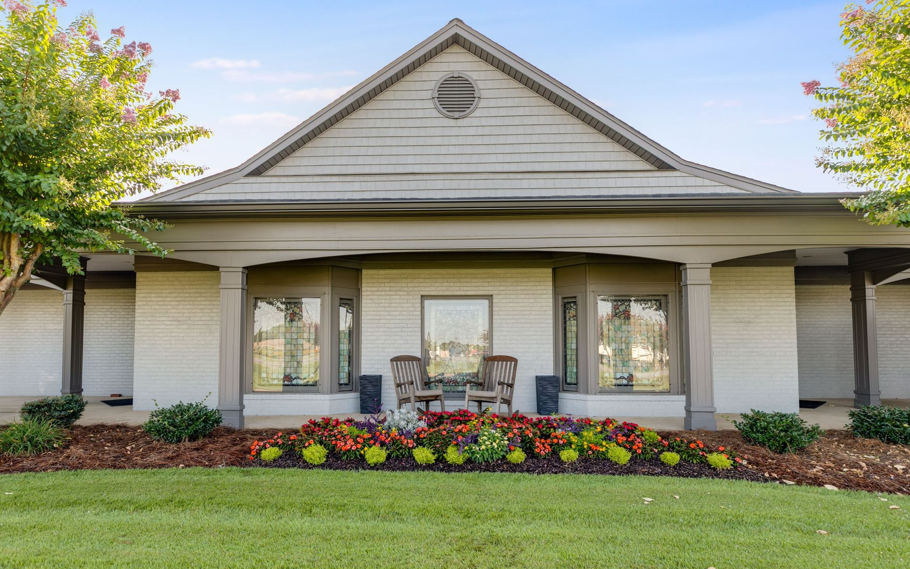 Single-story house with a front porch, white trim, and colorful flower bed in front.
