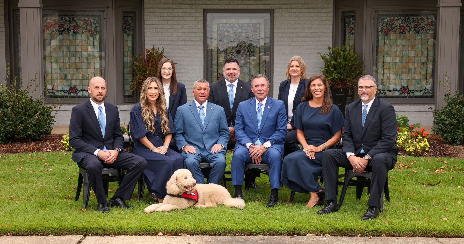 Formal group portrait of seven people and a dog seated and standing in front of a house