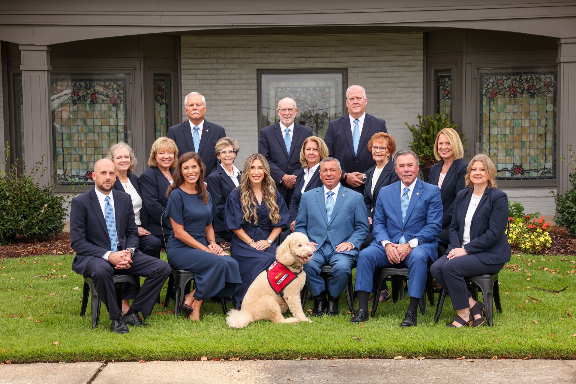Formal family group portrait outdoors in front of a house, with a cream-colored dog in front.
