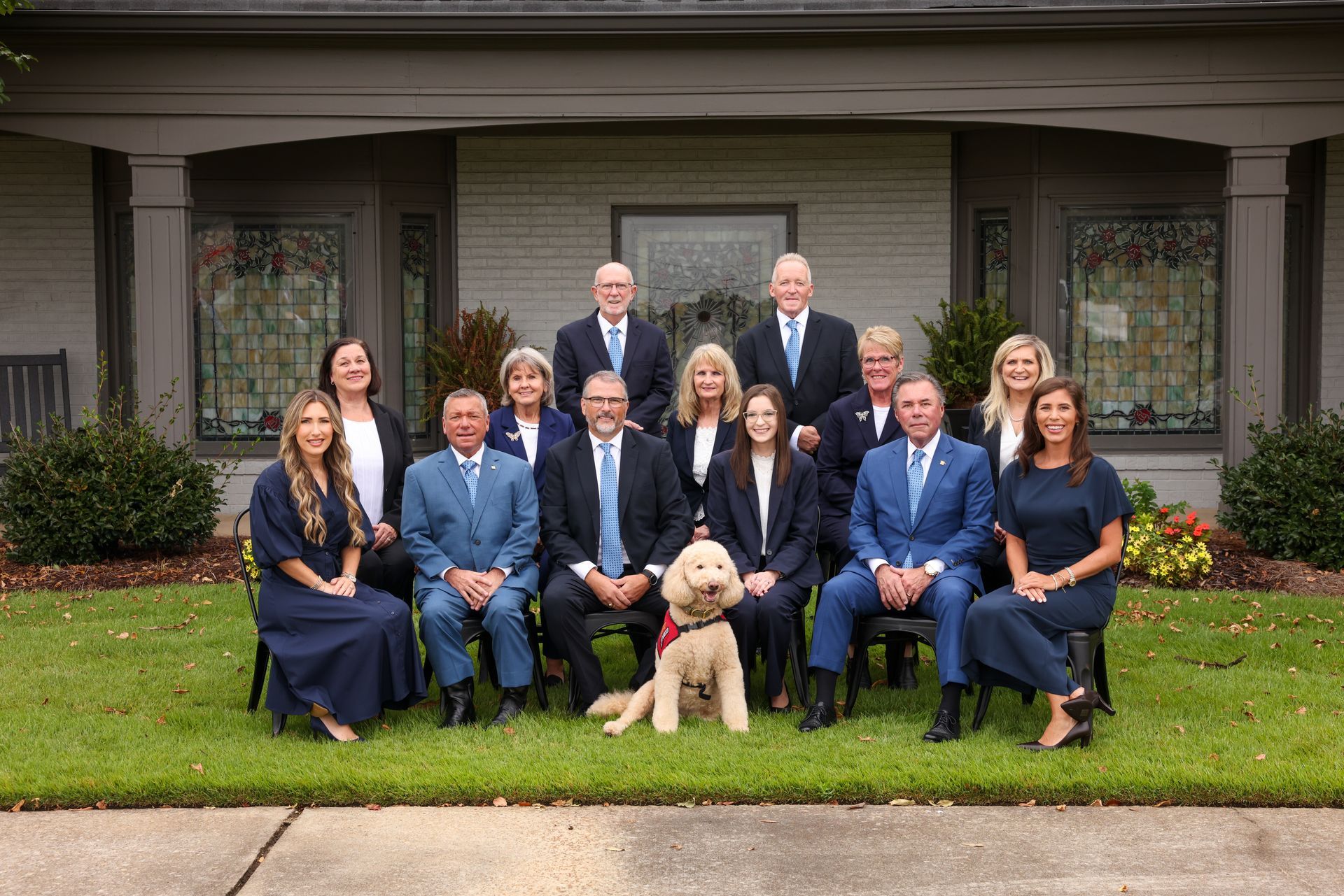 Formal group portrait of 12 people and a dog posed in front of a house