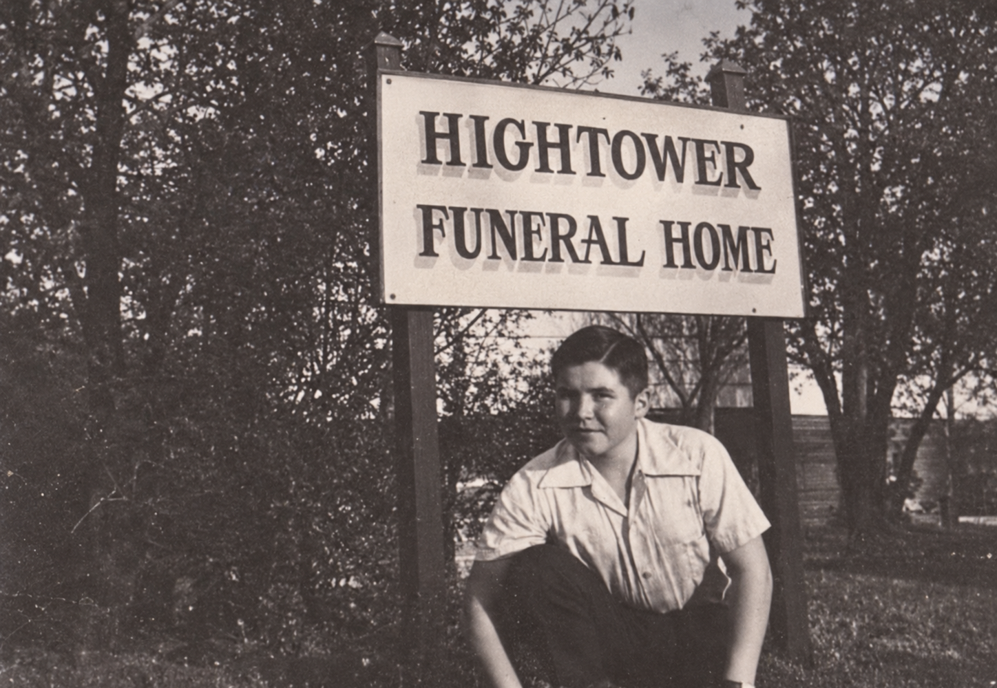 Person standing beside a “Hightower Funeral Home” sign outdoors.
