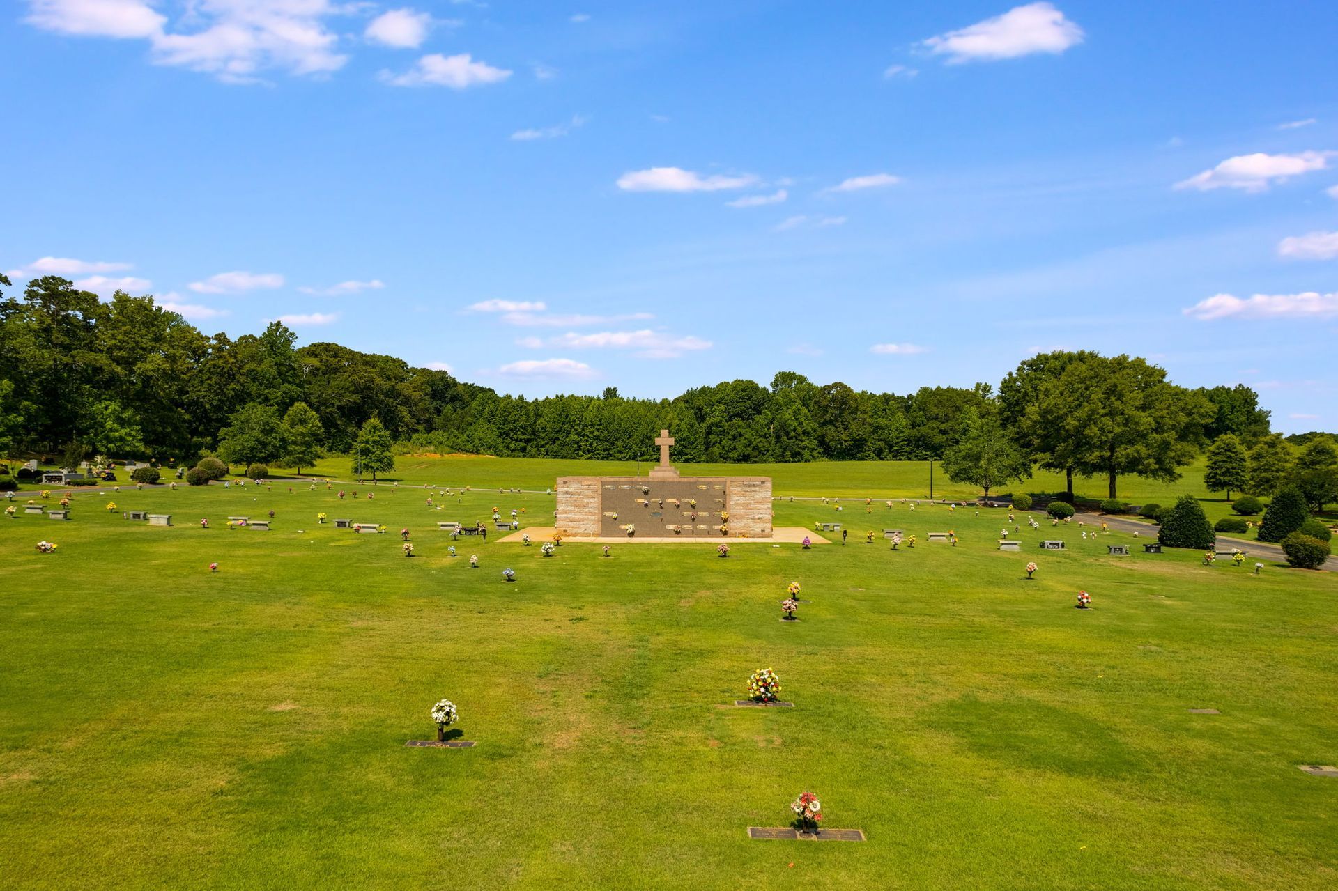 Grassy memorial park under blue sky with scattered headstones and a central monument