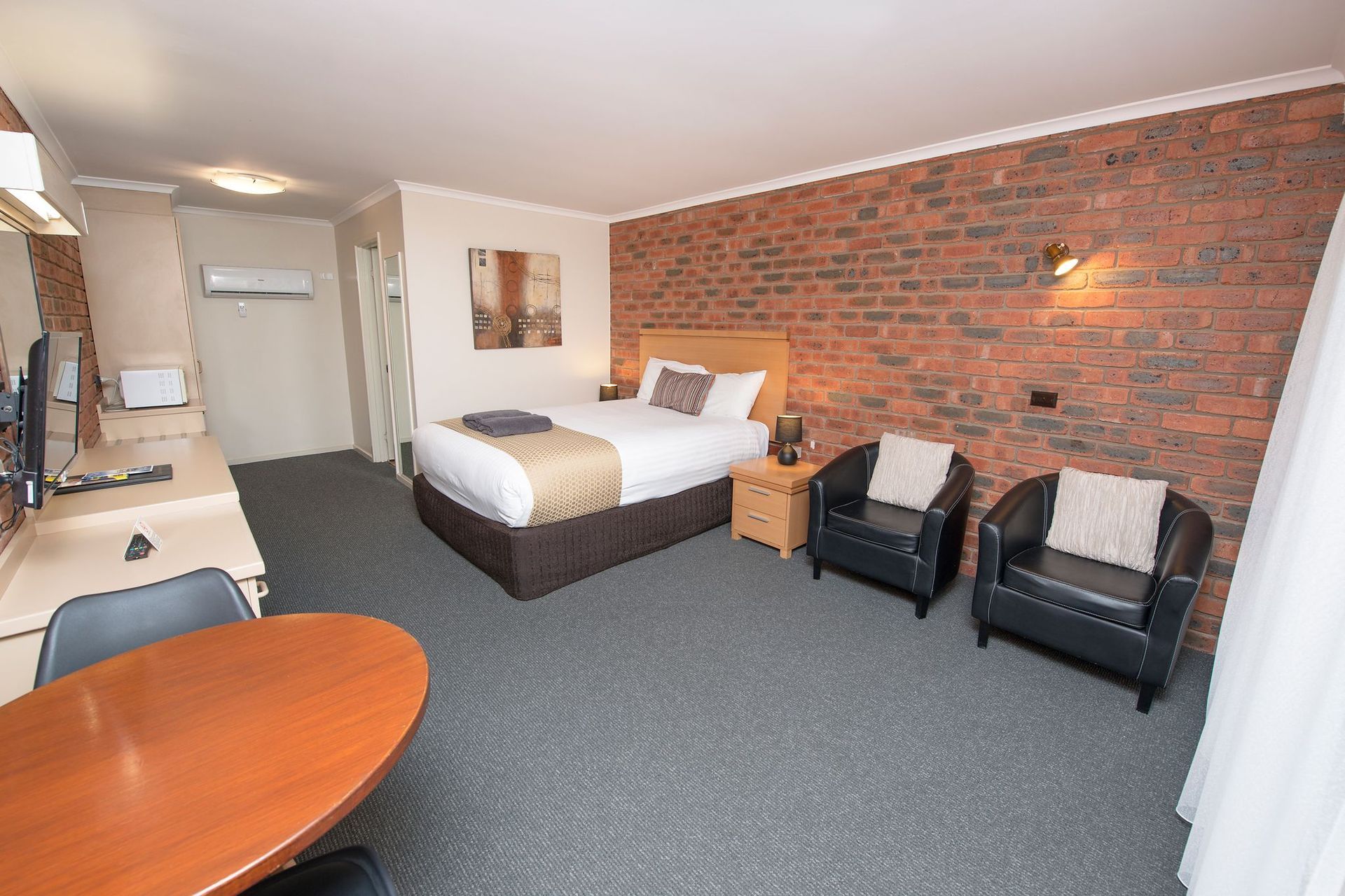 Hotel room with bed, chairs, exposed brick wall, and desk.