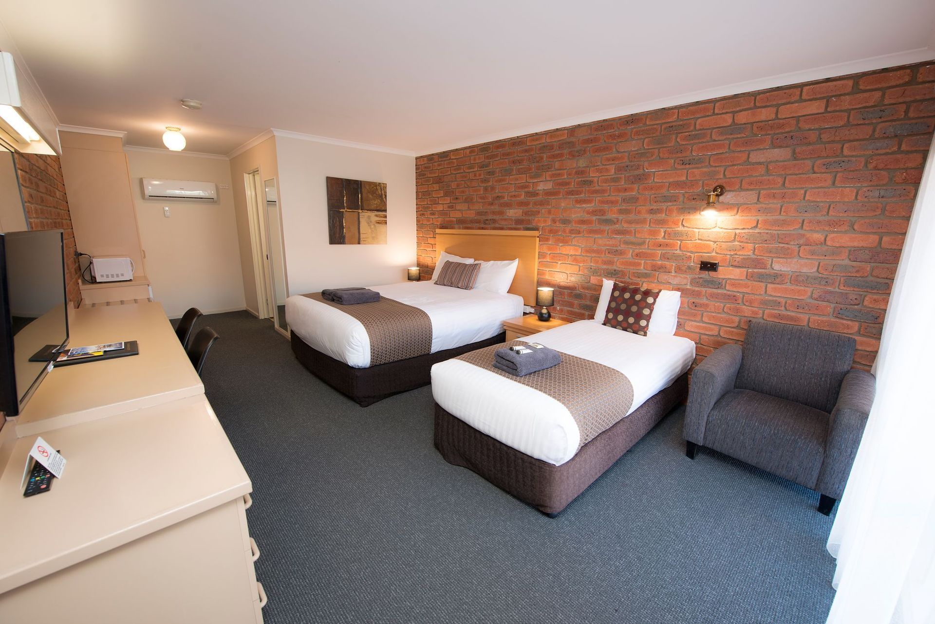 Hotel room with two beds, brick accent wall, chair, and TV.