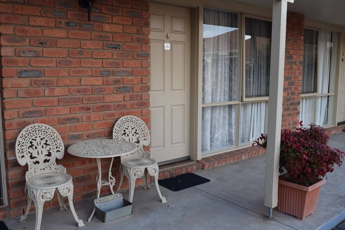 Motel exterior with brick wall, wrought-iron table and chairs, and window with curtains.