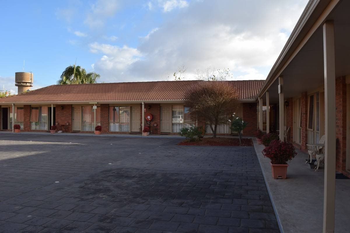 Motel exterior with a red tiled roof, brown brick walls, and a water tower in the distance.