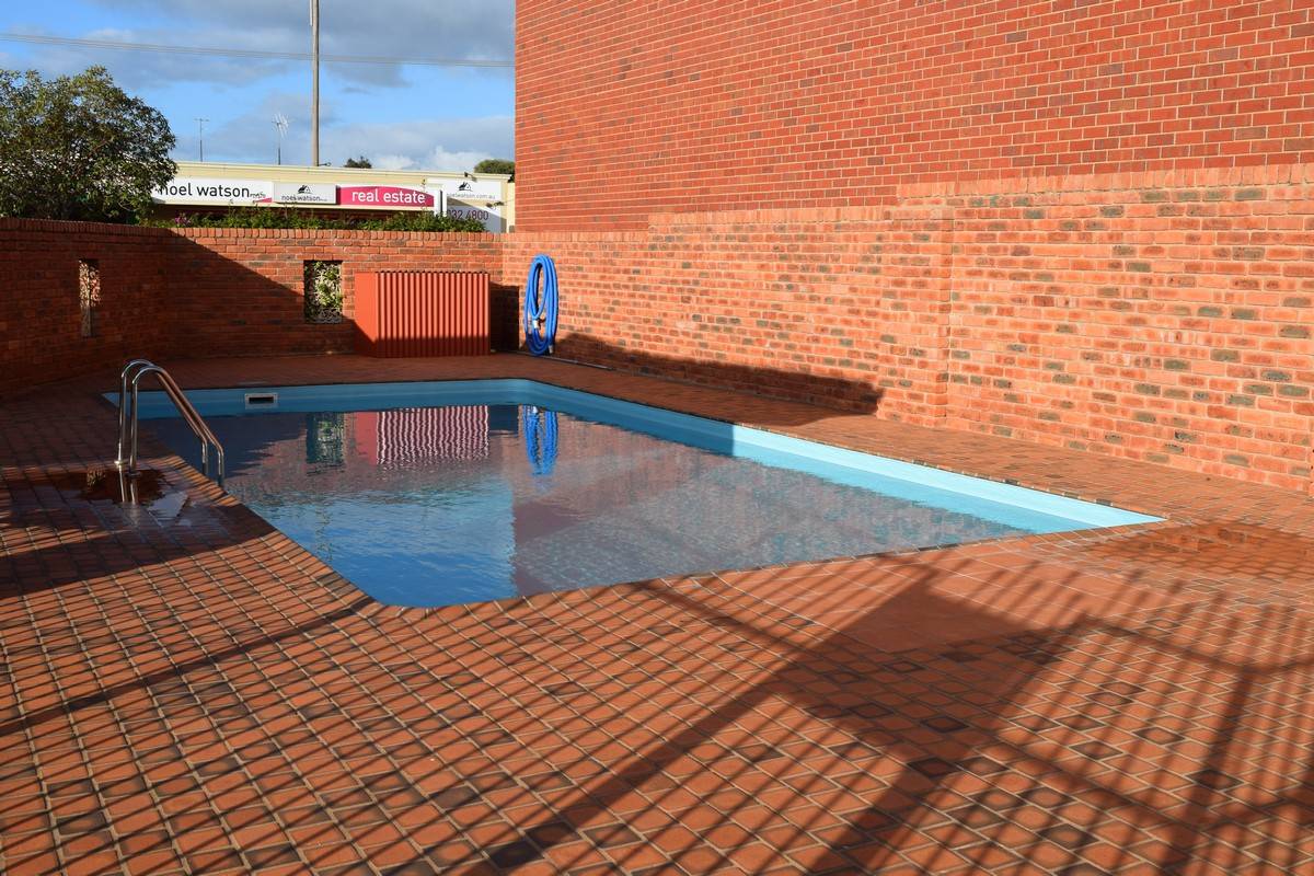 Brick-lined outdoor swimming pool surrounded by red brick walls on a sunny day.