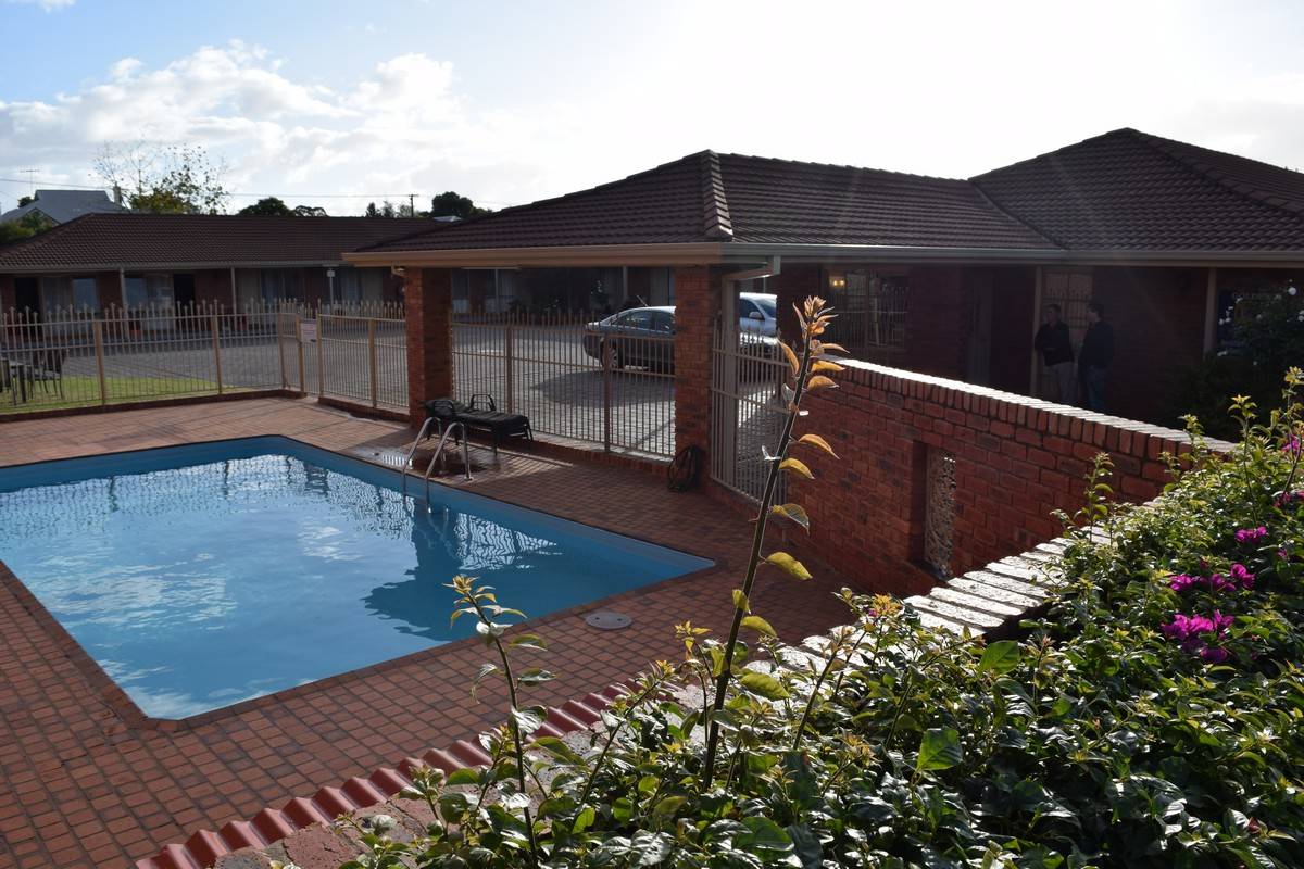 Pool and brick patio in front of a low-rise brick building with tiled roofs.