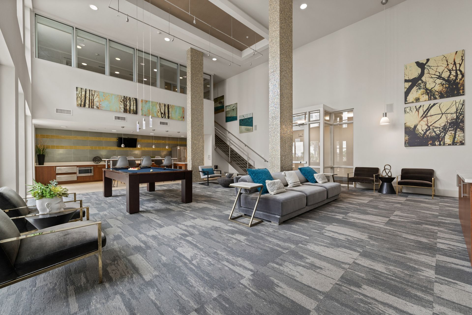 Modern lobby with high ceilings, gray seating, a pool table, and a staircase in a bright, airy interior at Sabina in Austin, TX.