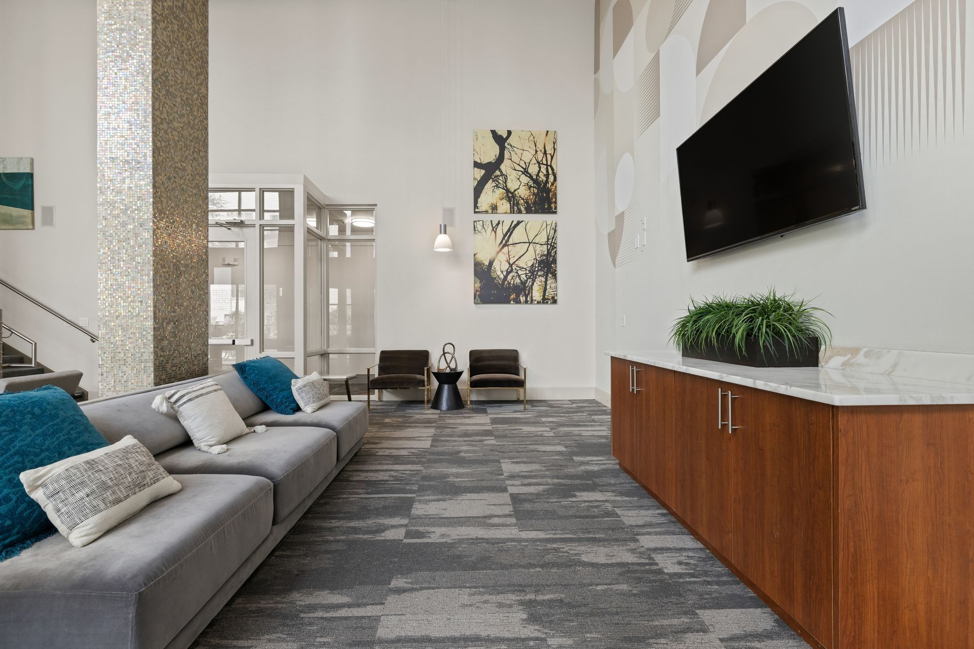 Modern clubhouse with gray sofa, wall-mounted TV, patterned rug, and wood console with plant at Sabina in Austin, TX.
