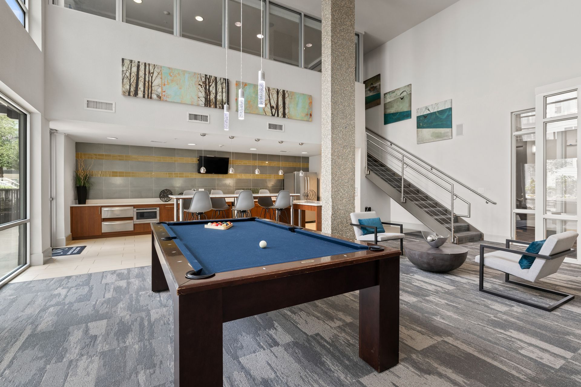 Modern loft game room with a pool table, kitchen, stairs, and lounge seating at Sabina in Austin, TX.