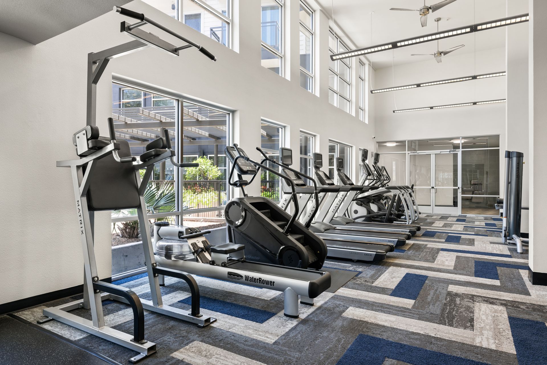 Bright modern gym with treadmills, ellipticals, and weight machines by large windows