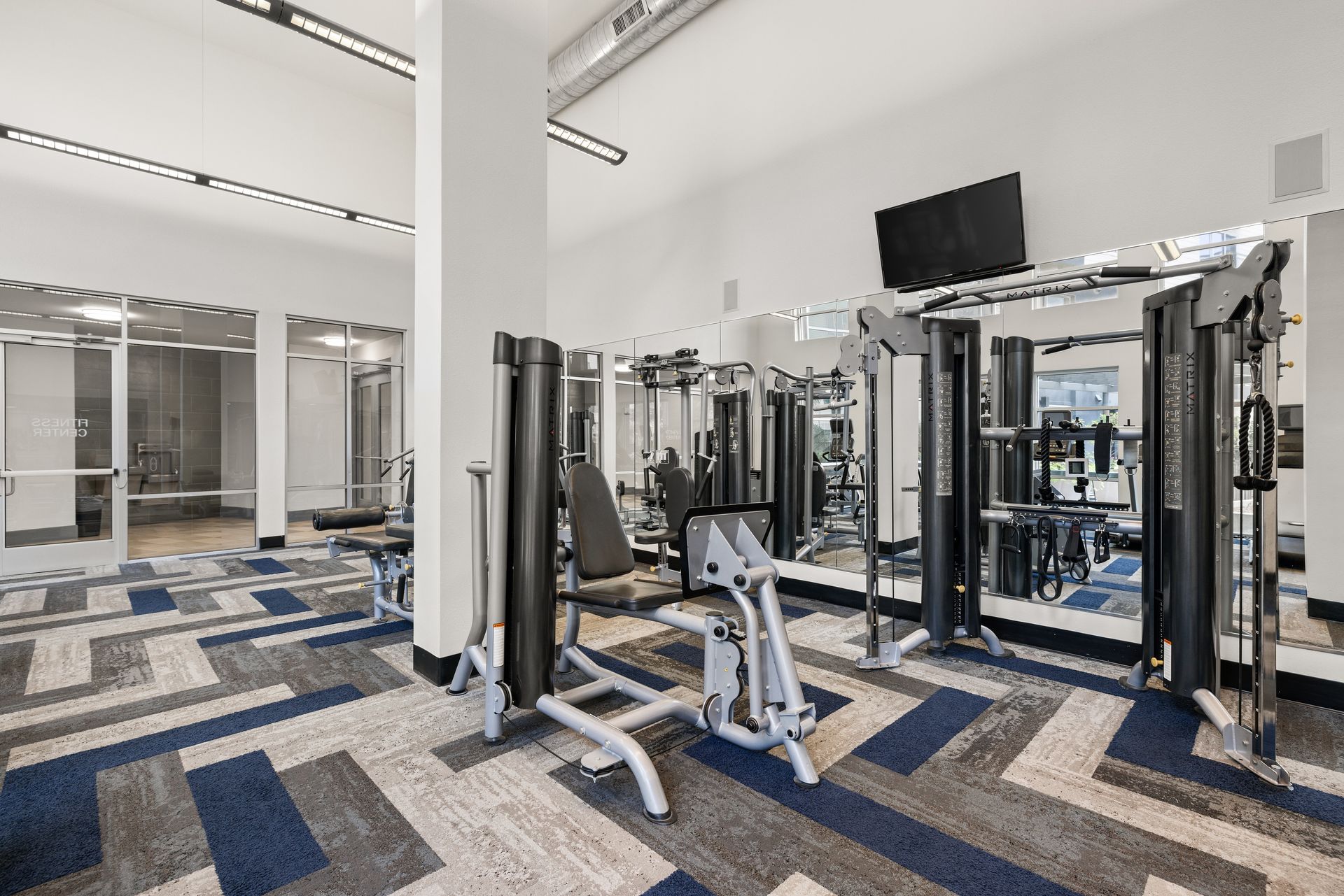 Modern gym interior with weight machines, mirrors, and blue-gray carpet tiles