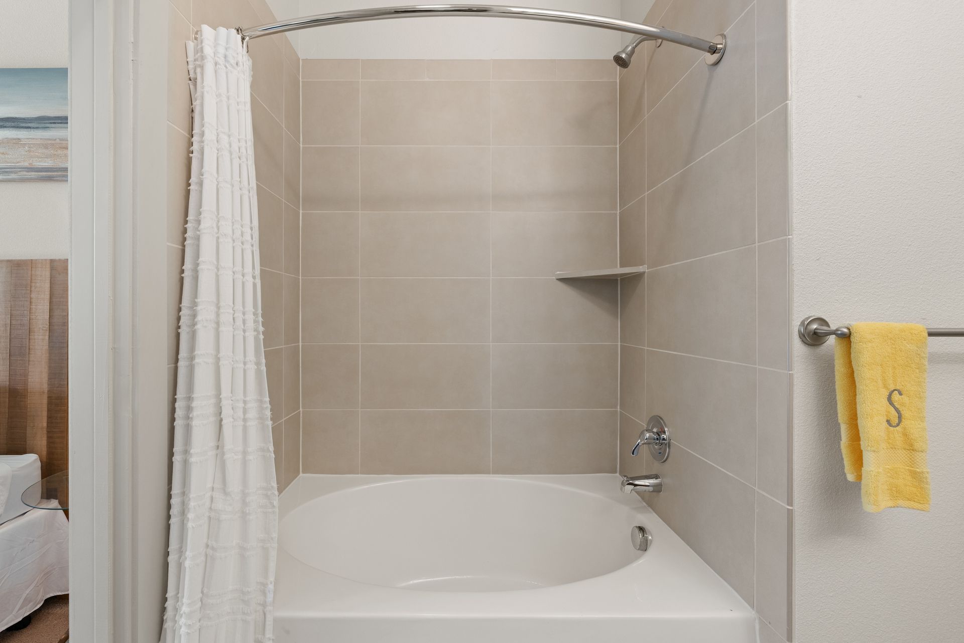 Small beige-tiled bathtub shower with white curtain and yellow hand towel in a bathroom at Sabina in Austin, TX.