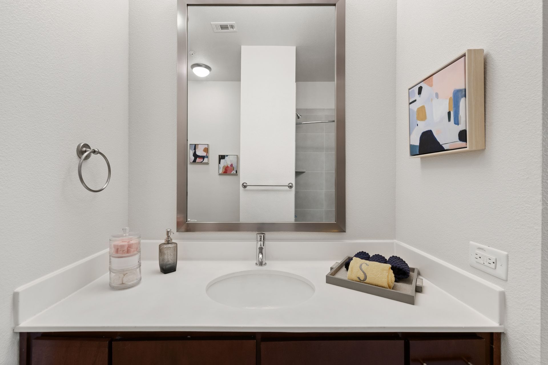 Bathroom vanity with mirror, sink, soap dispenser, towel ring, and wall art at Sabina in Austin, TX.