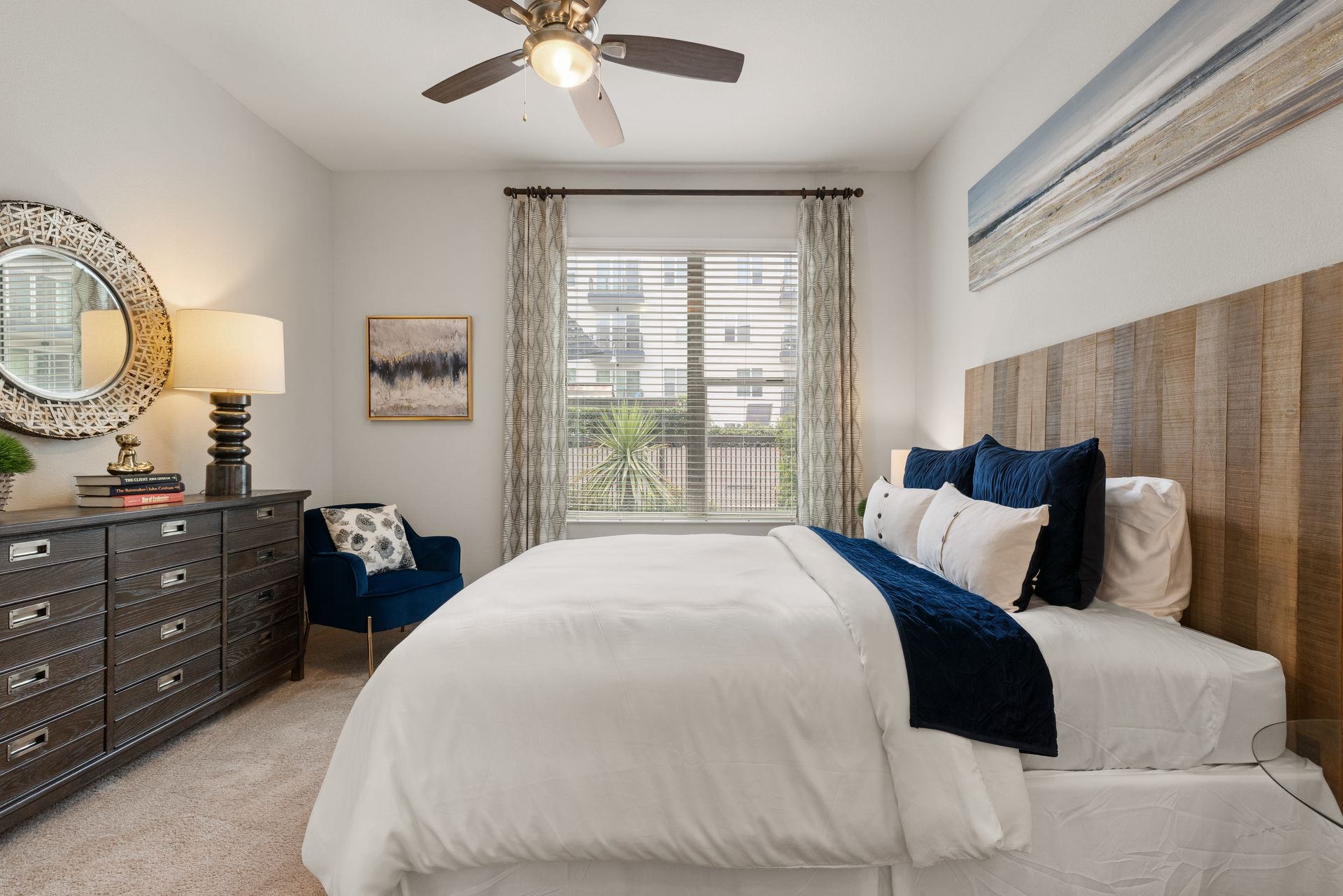 Bright bedroom with a white bed, navy accents, dresser, and large window with blinds at Sabina in Austin, TX.