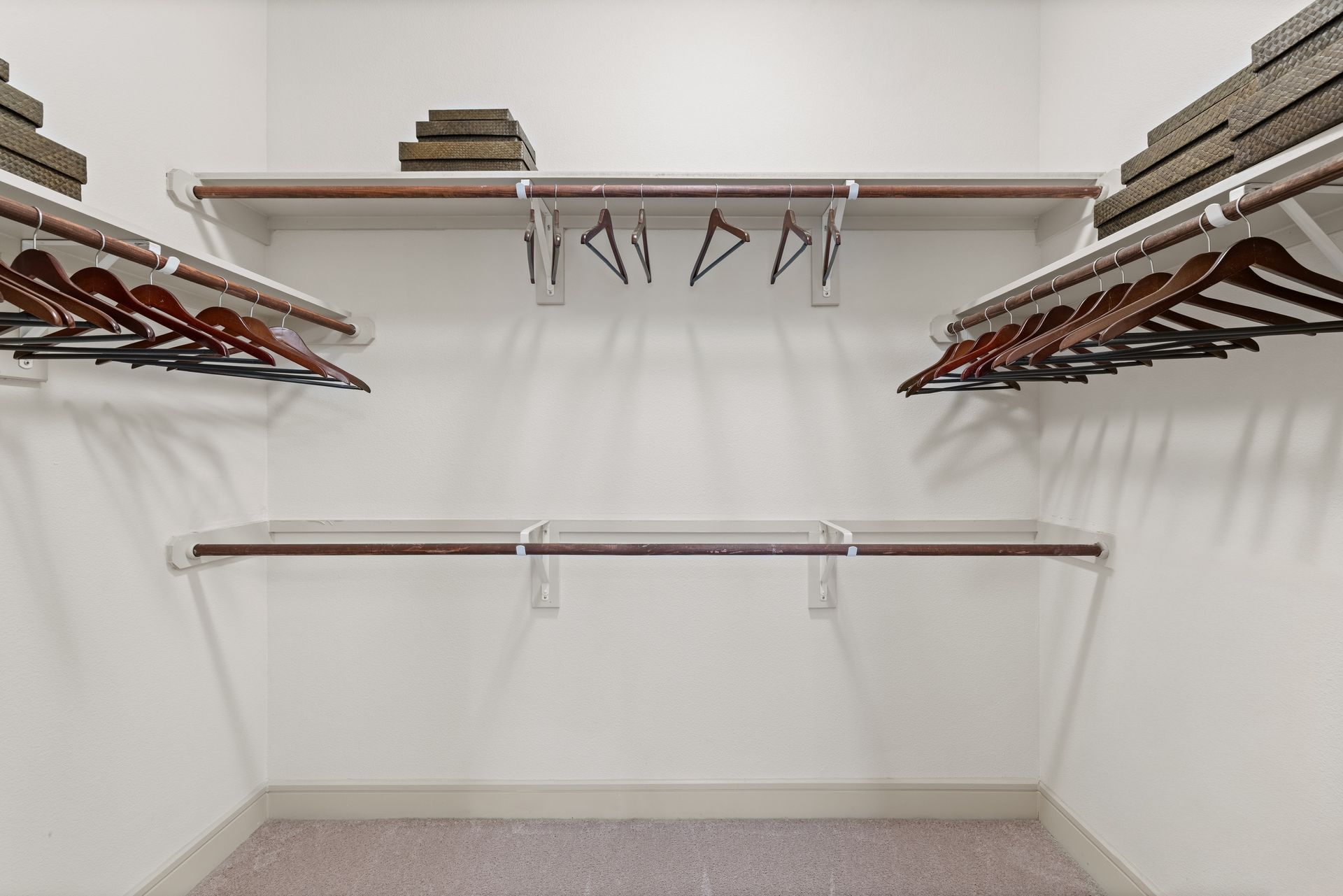 Empty walk-in closet with wooden hanging rods, wire shelves, and a few empty hangers at Sabina in Austin, TX.