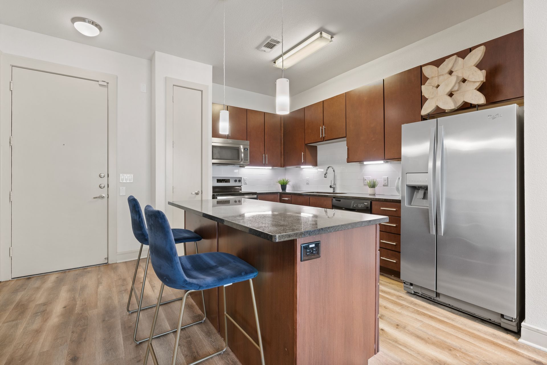 Modern kitchen with stainless steel appliances, wood cabinets, island seating, and light wood floors