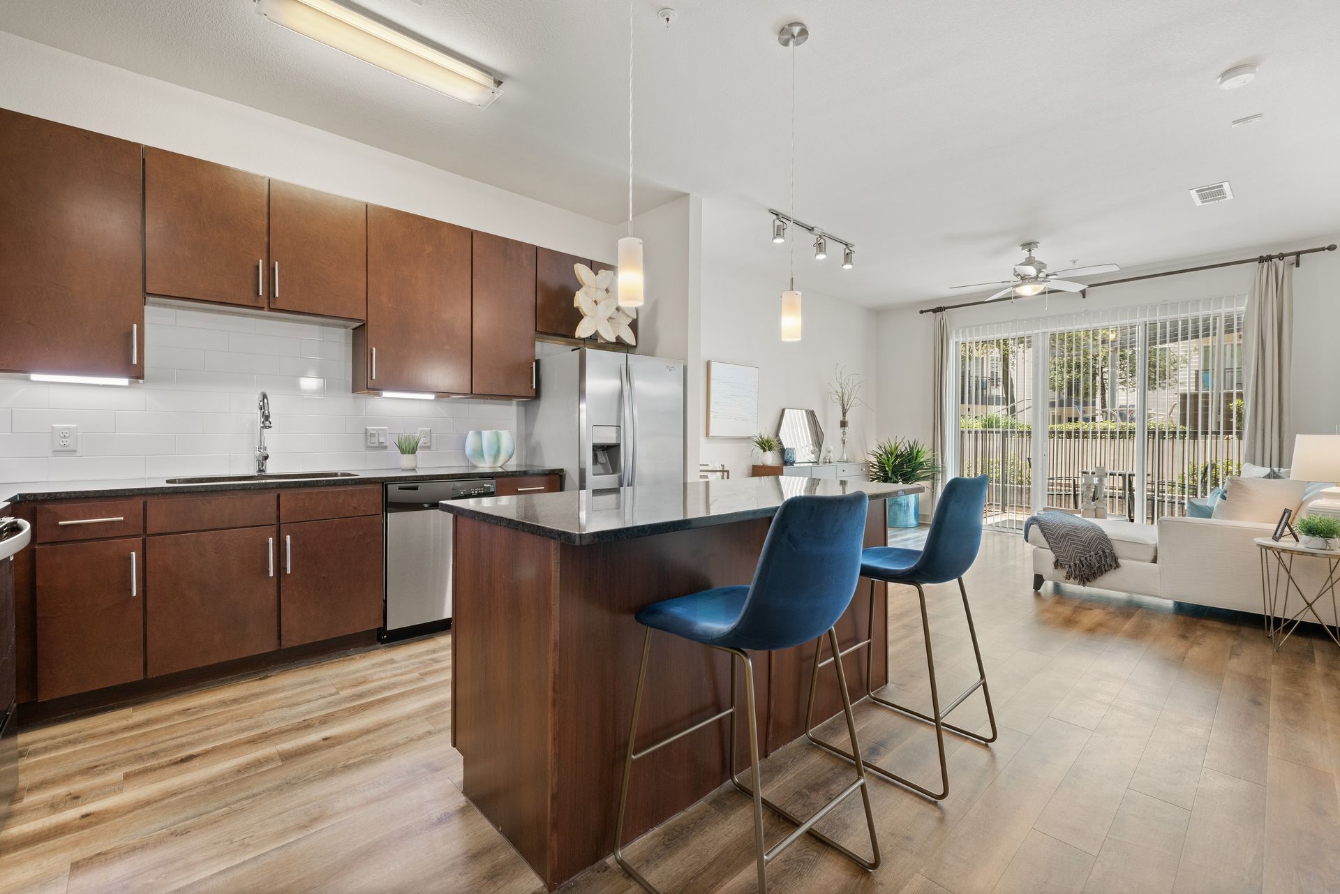 Modern kitchen with wood cabinets, island seating, and a bright open living area by sliding glass doors
