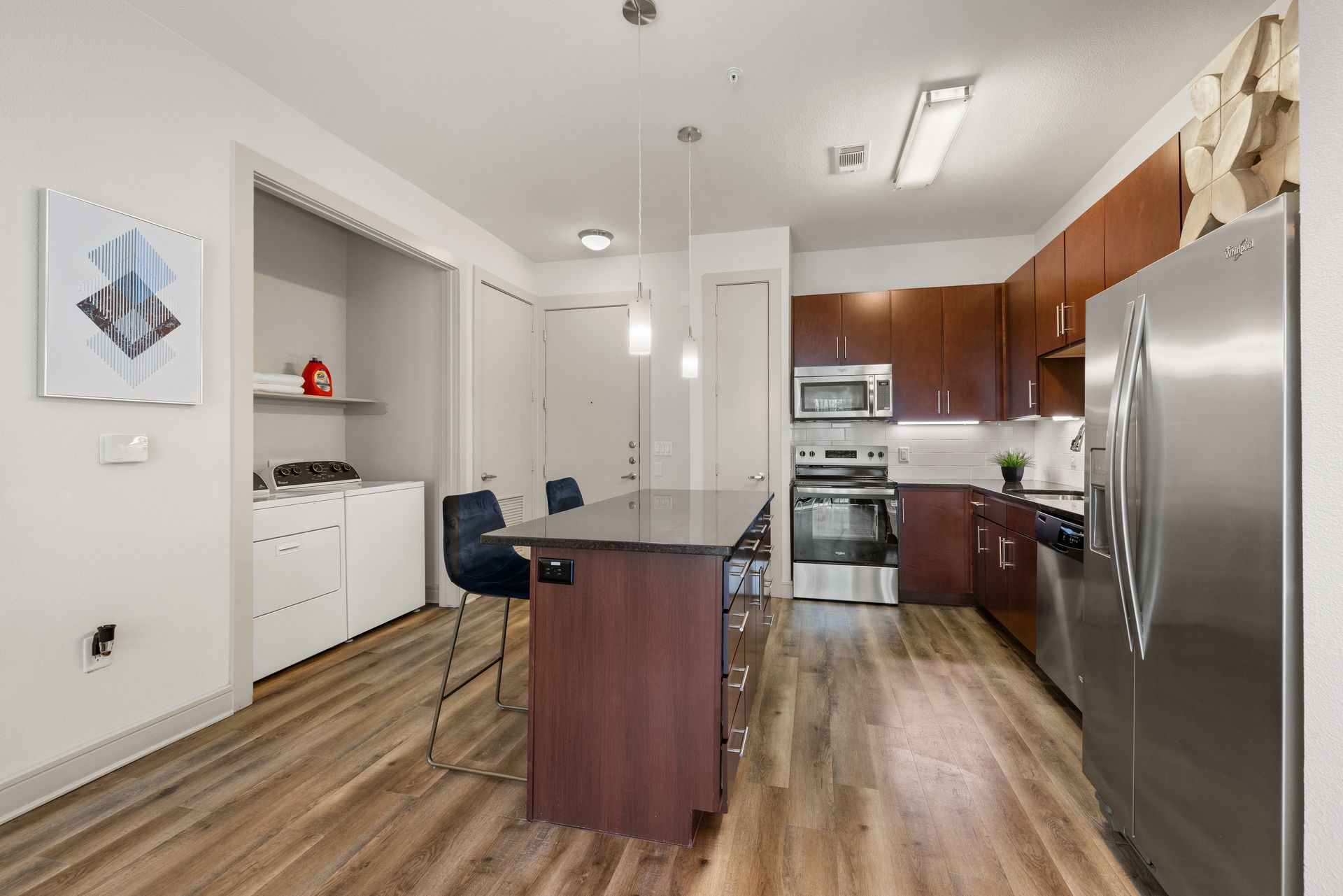Modern kitchen with stainless steel appliances, dark wood cabinets, and a central island on wood flooring
