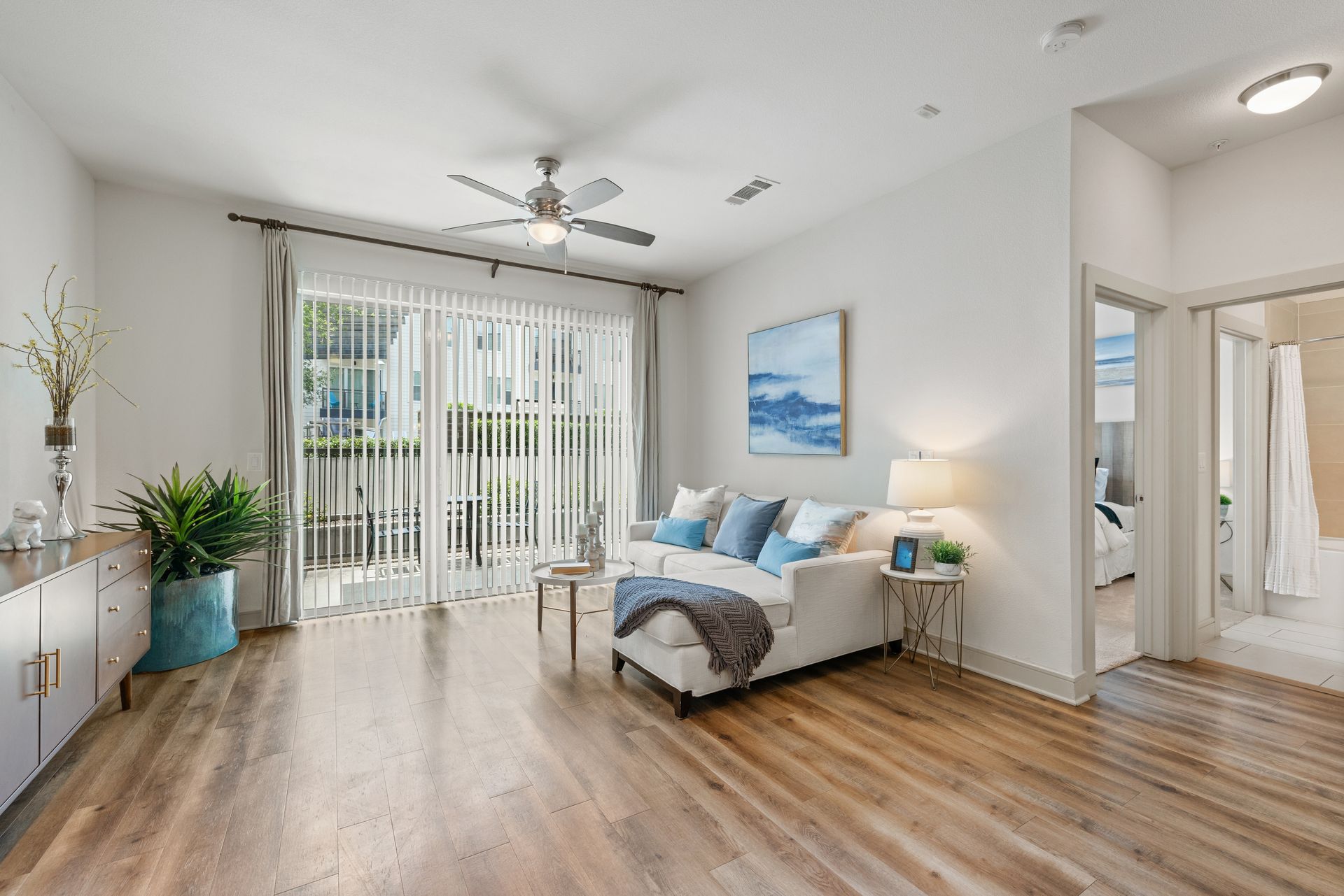 Bright modern bedroom with bed, sliding glass doors, wood floors, and a ceiling fan at Sabina in Austin, TX.